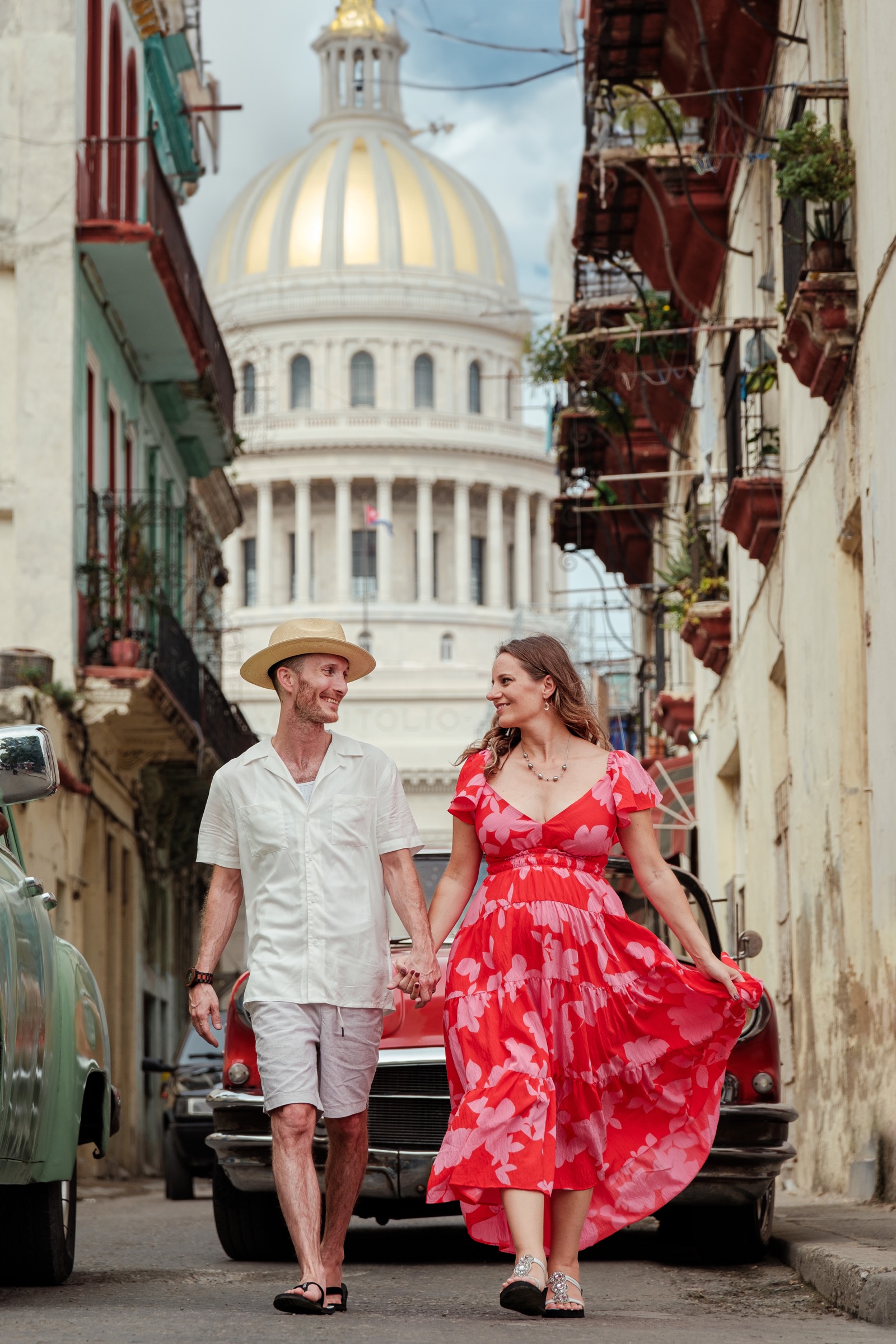 A couple walking hand in hand down a Havana street with the Capitolio dome rising behind them