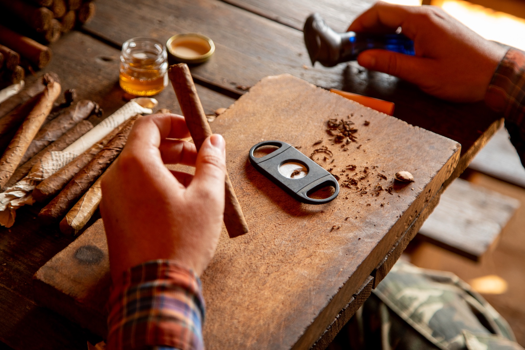 A guillotine cutter, fresh cigars and a glass of rum on a rustic wooden table