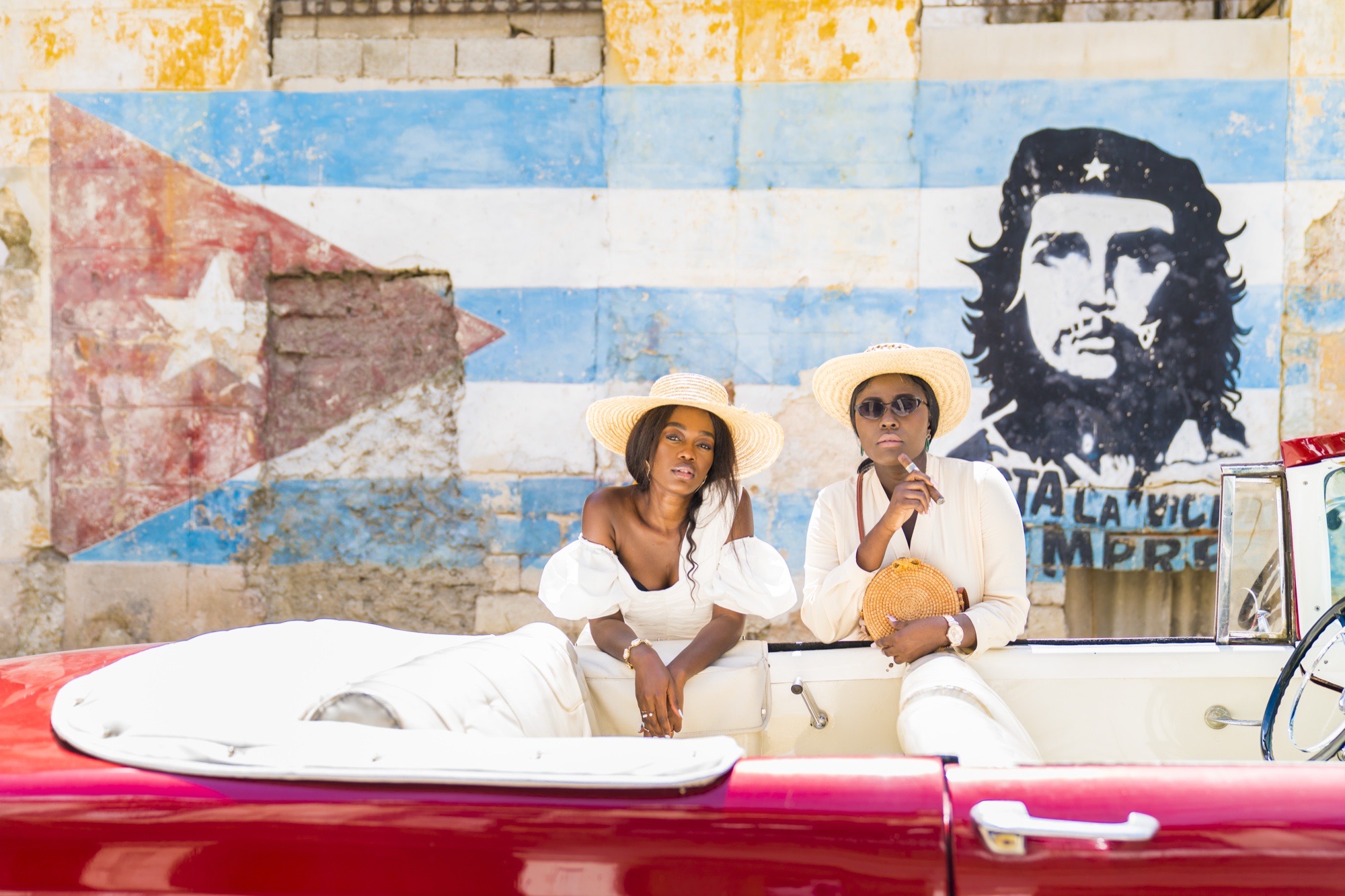 Two guests in a classic convertible in front of a painted Cuban flag wall