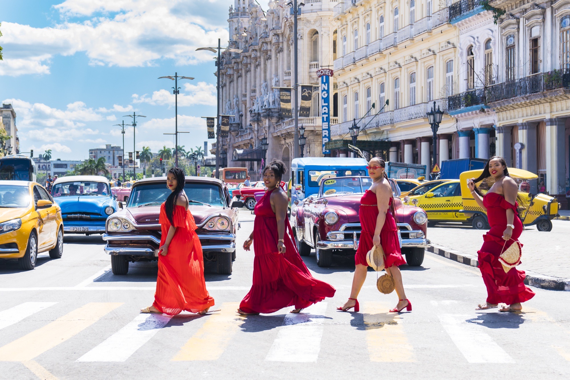 Four guests in red dresses crossing a Havana street lined with classic cars