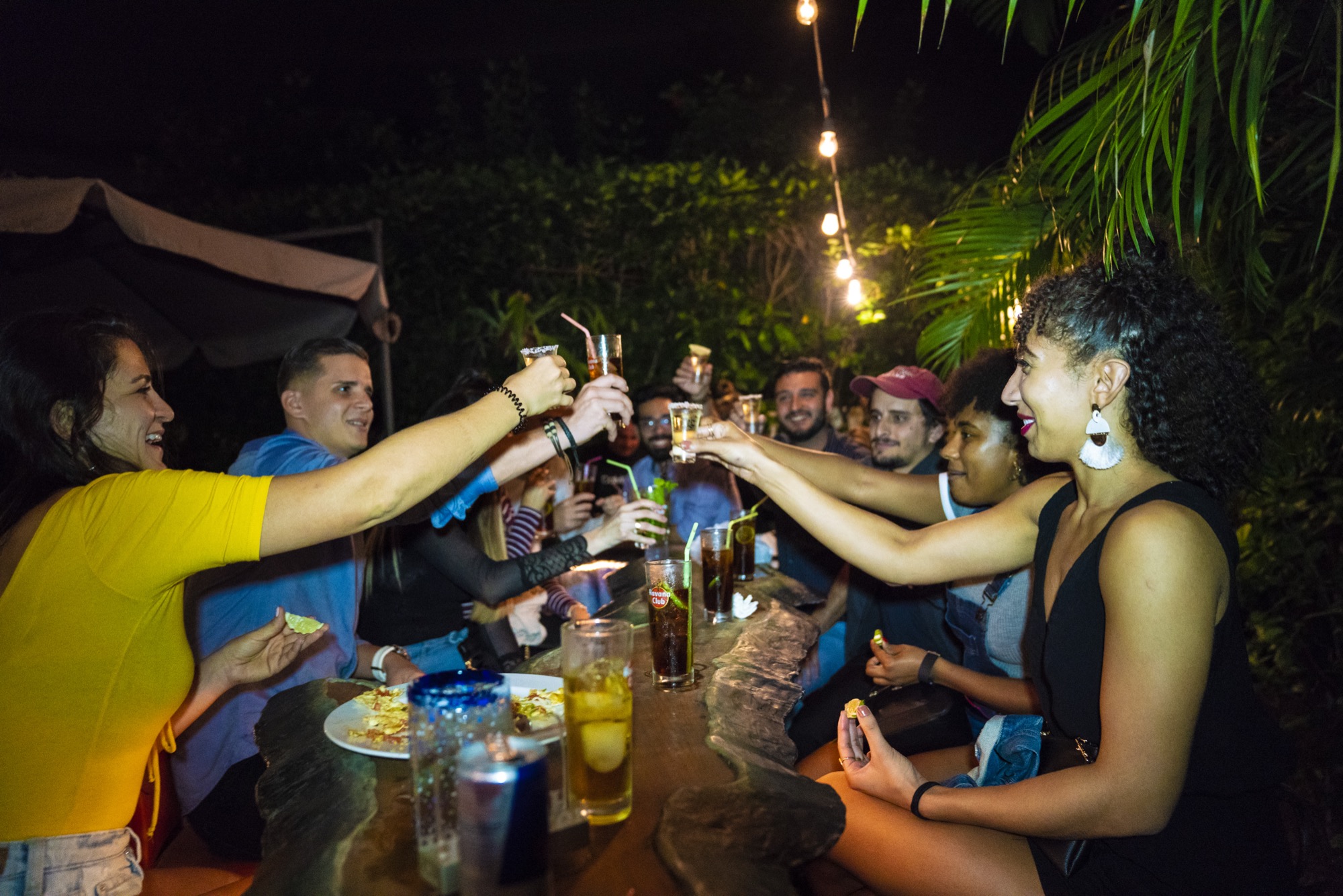 A long candlelit table of friends mid-toast on a Havana patio at night