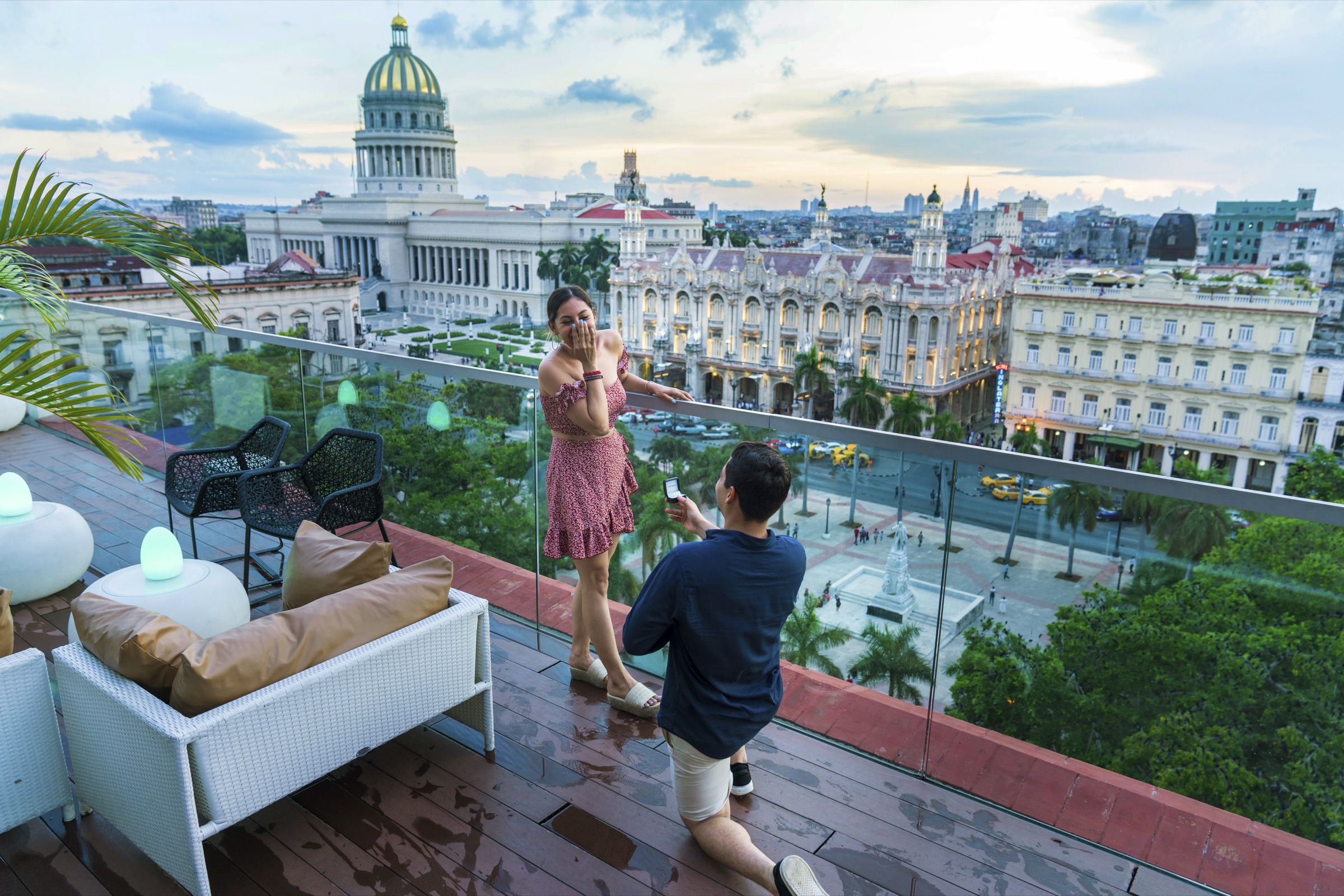 A newly engaged couple celebrating on a rooftop terrace with the Capitolio dome and the Havana skyline spread out behind them