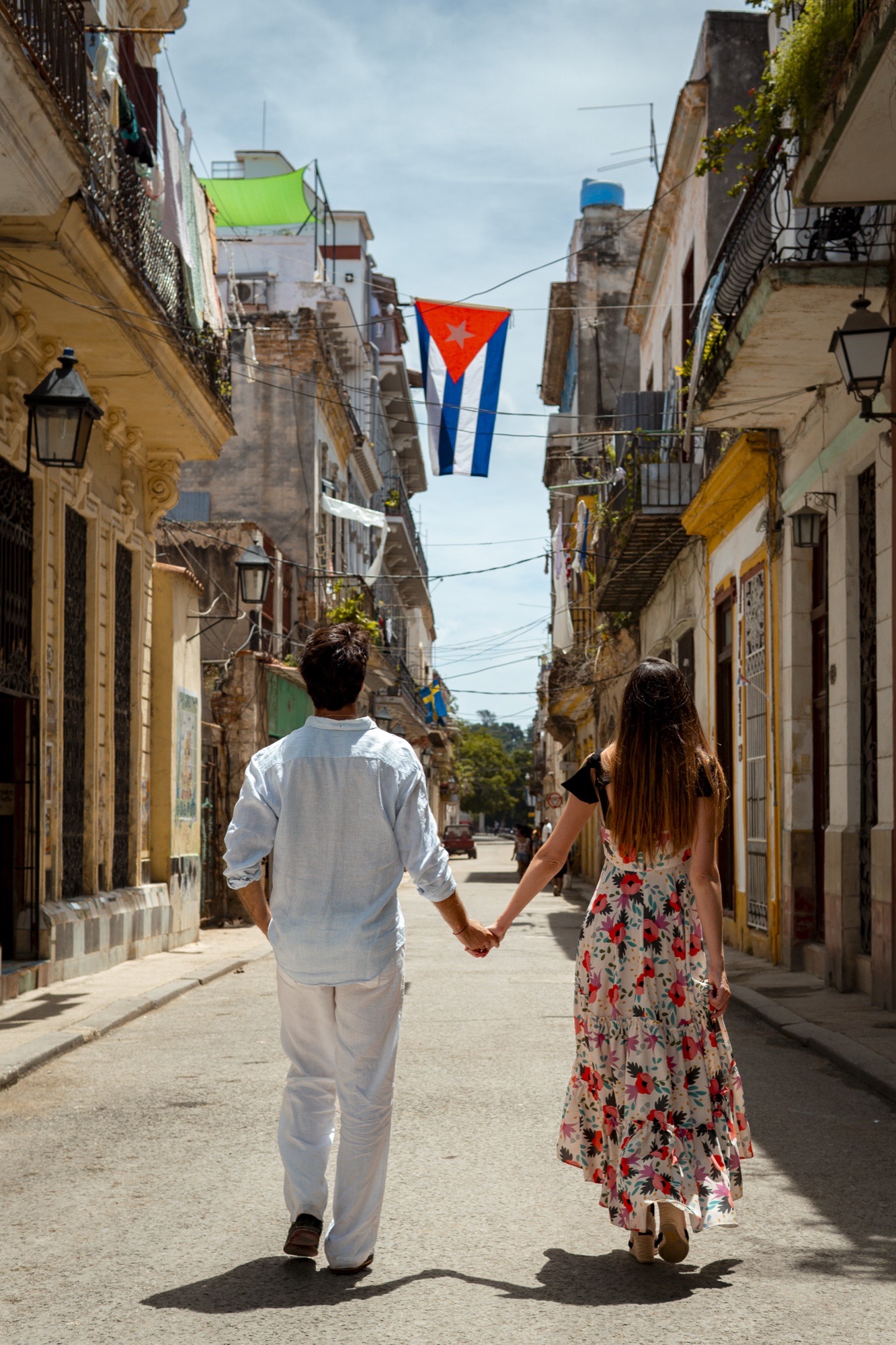 A couple walking hand in hand down a Havana street beneath a Cuban flag