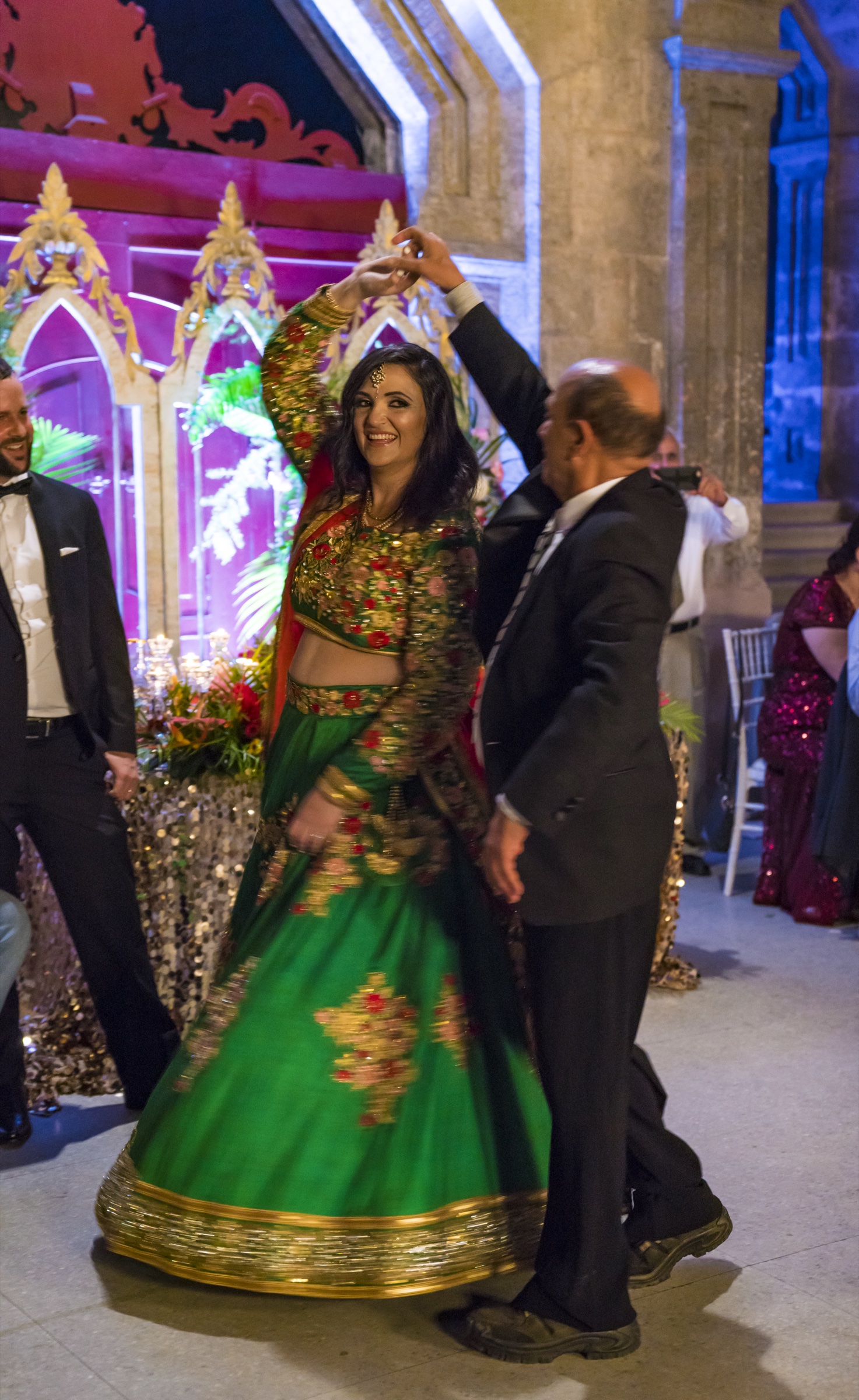 The bride in a green and gold lehenga twirling as she dances with her father in a chandelier-lit colonial courtyard at night