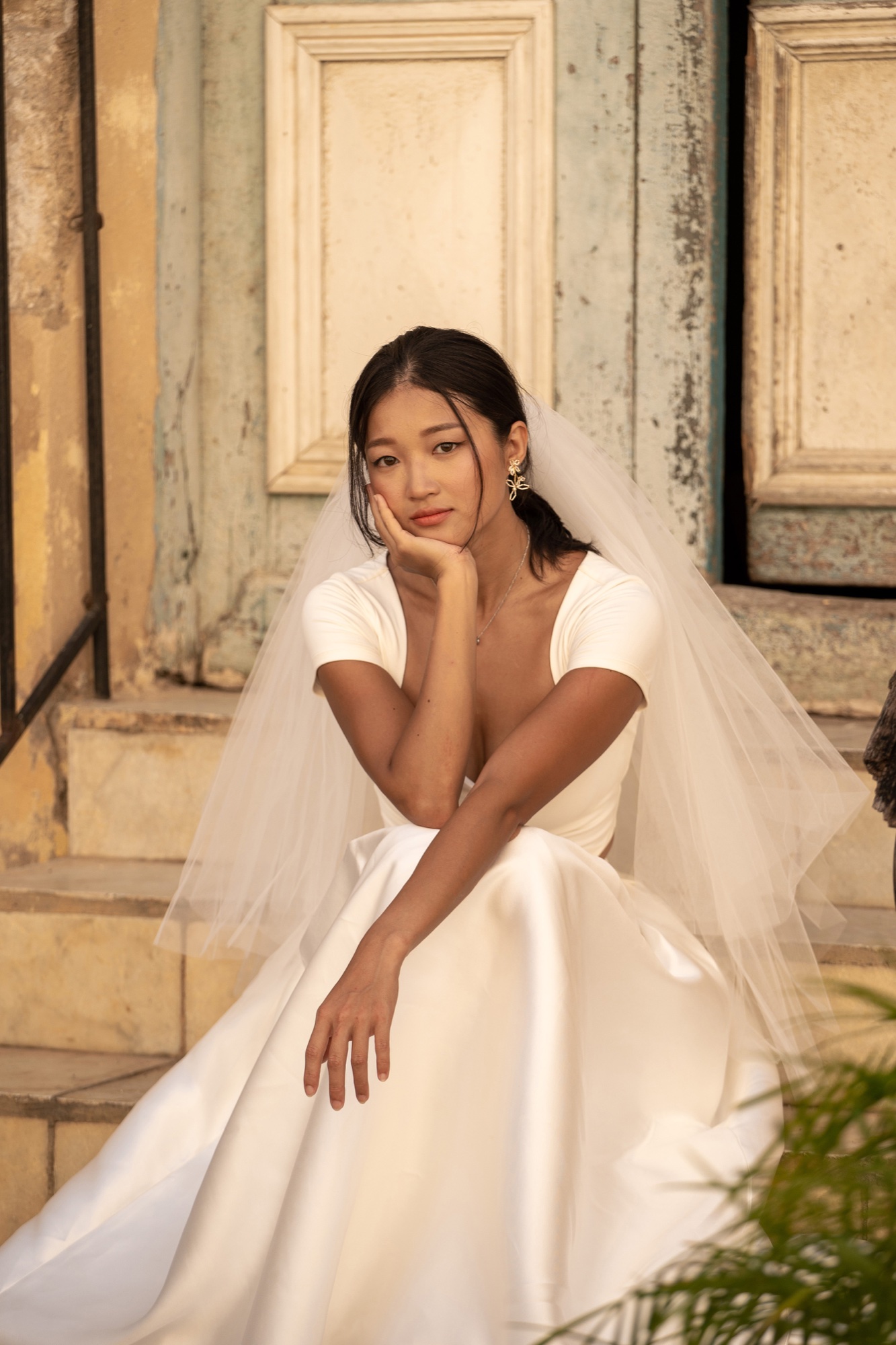 A bride in a veil sitting on the worn stone steps of an old Havana doorway in golden light