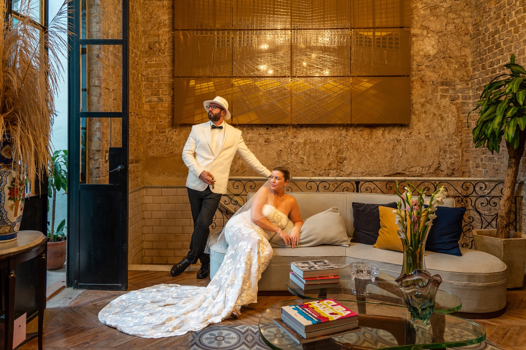 A groom in a white dinner jacket standing beside his bride, her lace train spread across the floor of a restored Old Havana interior