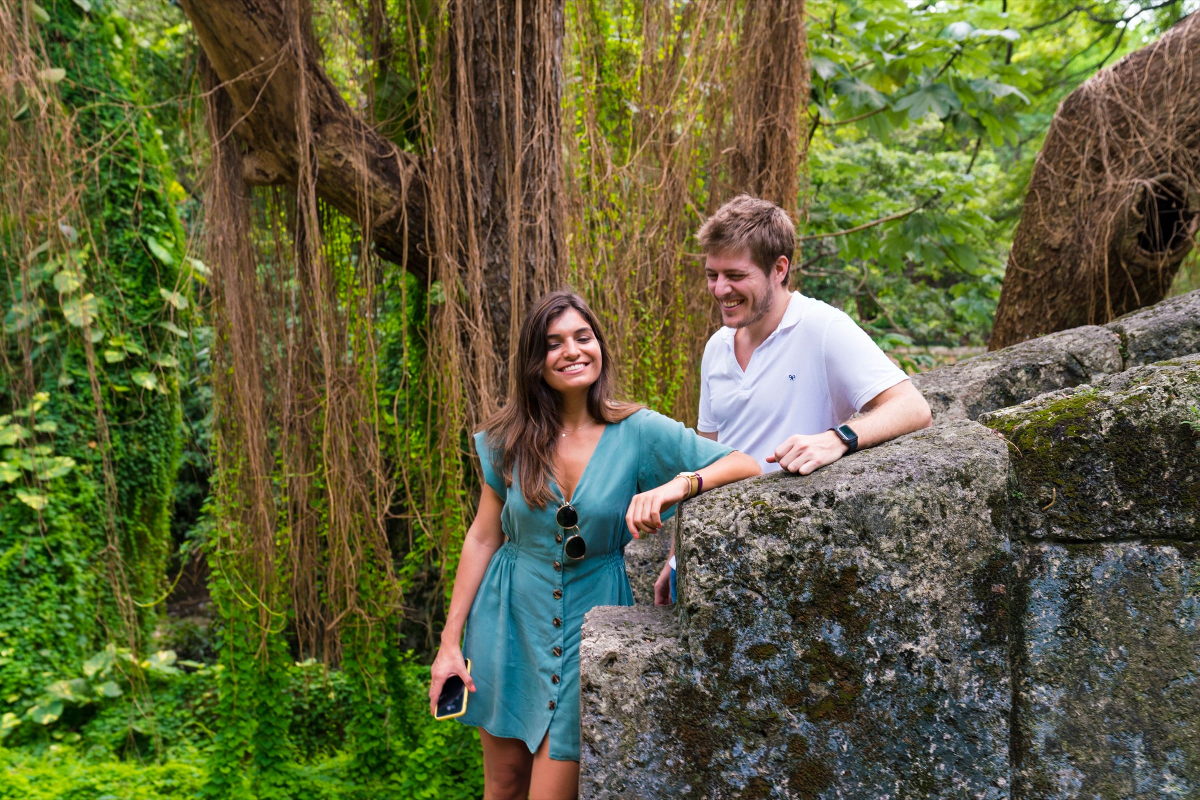 A couple leaning on an old stone bridge surrounded by lianas