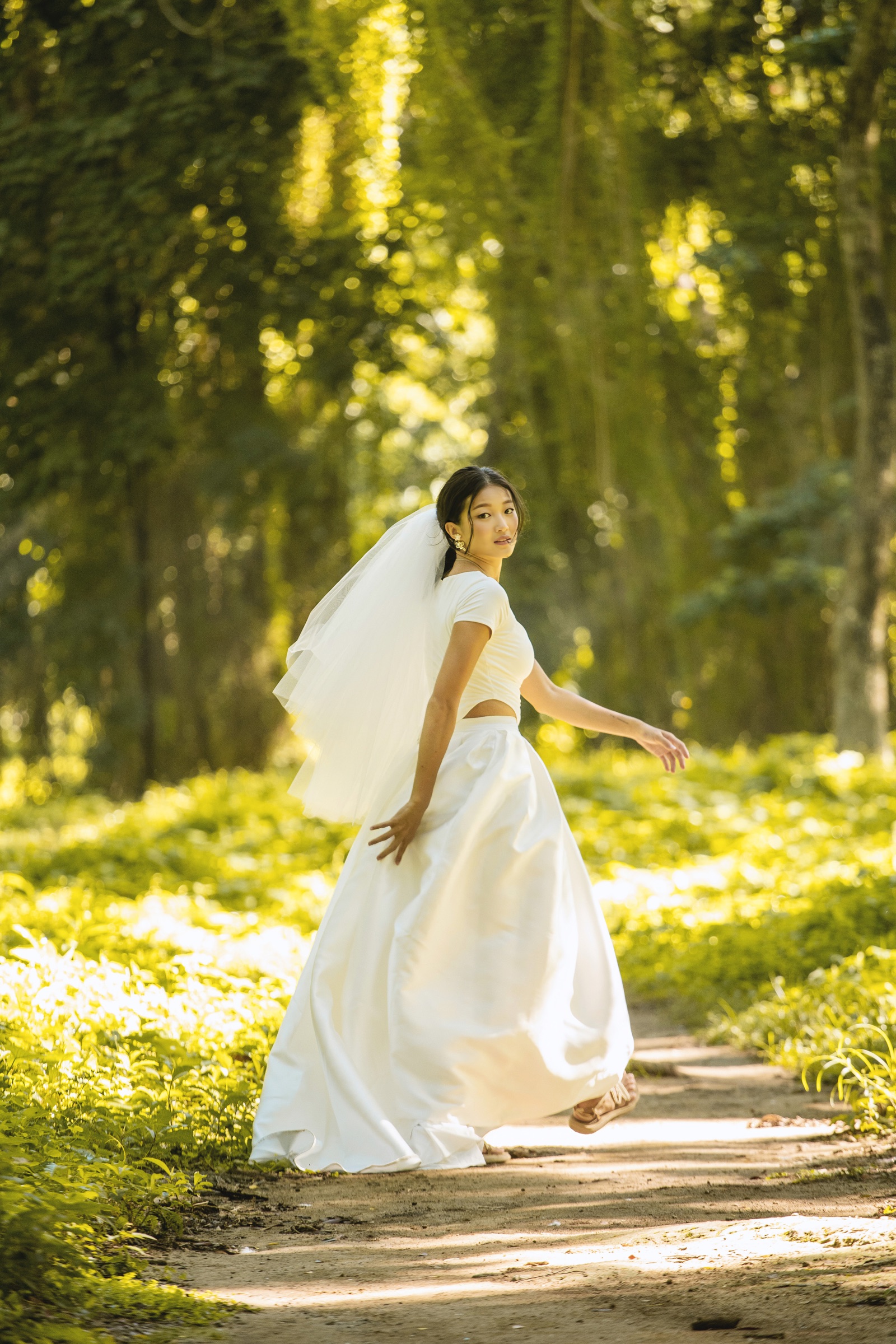 A bride in a veil turning on a sunlit forest path