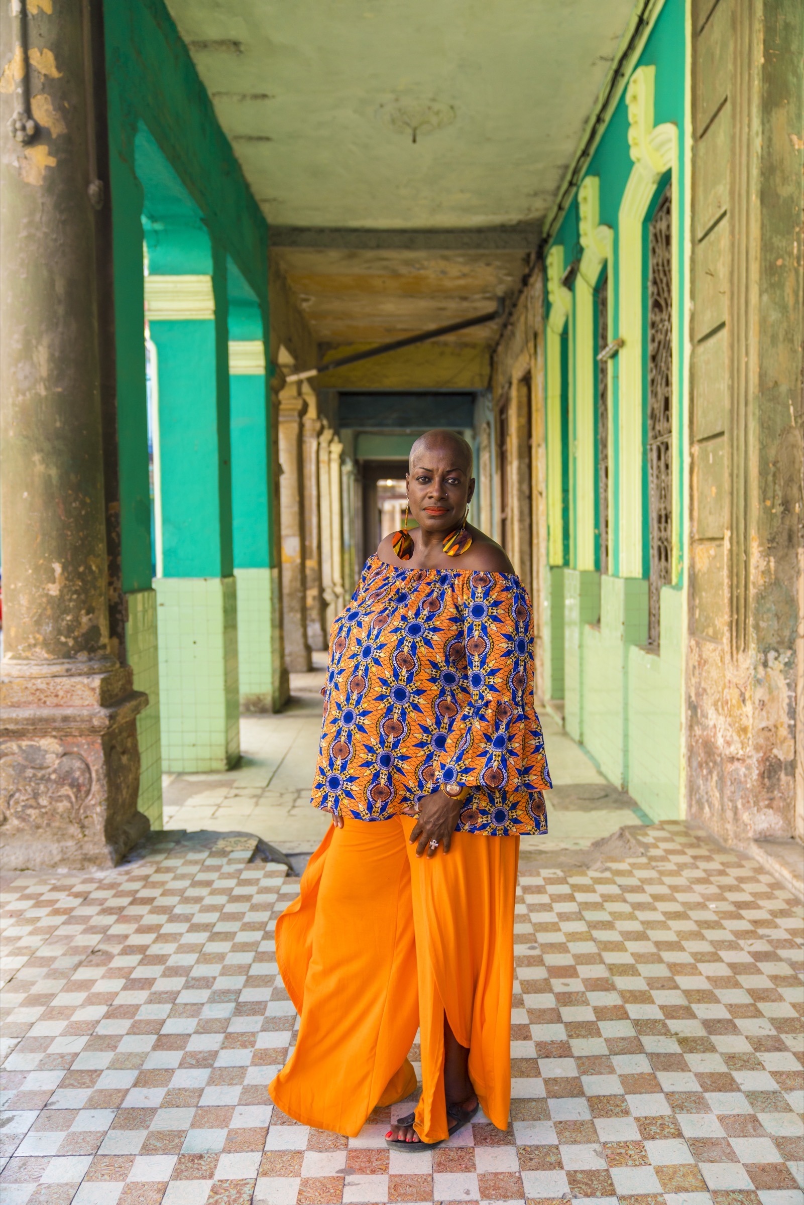 A woman in orange standing in a colonnaded arcade with green columns
