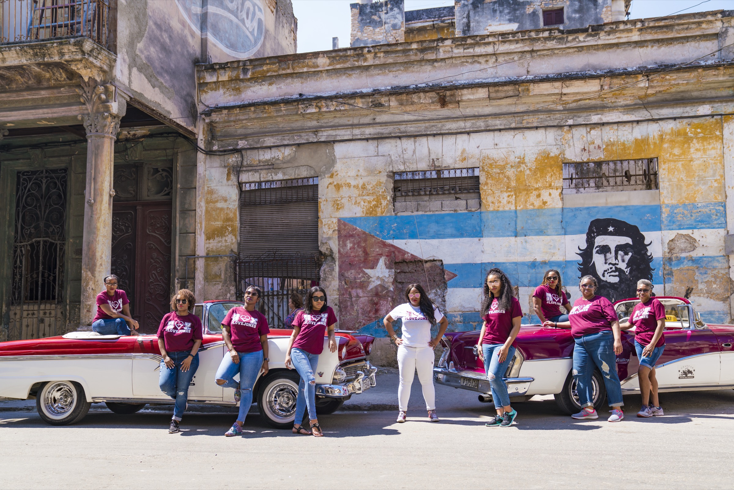 A large group with two classic cars in front of the flag-and-Che mural