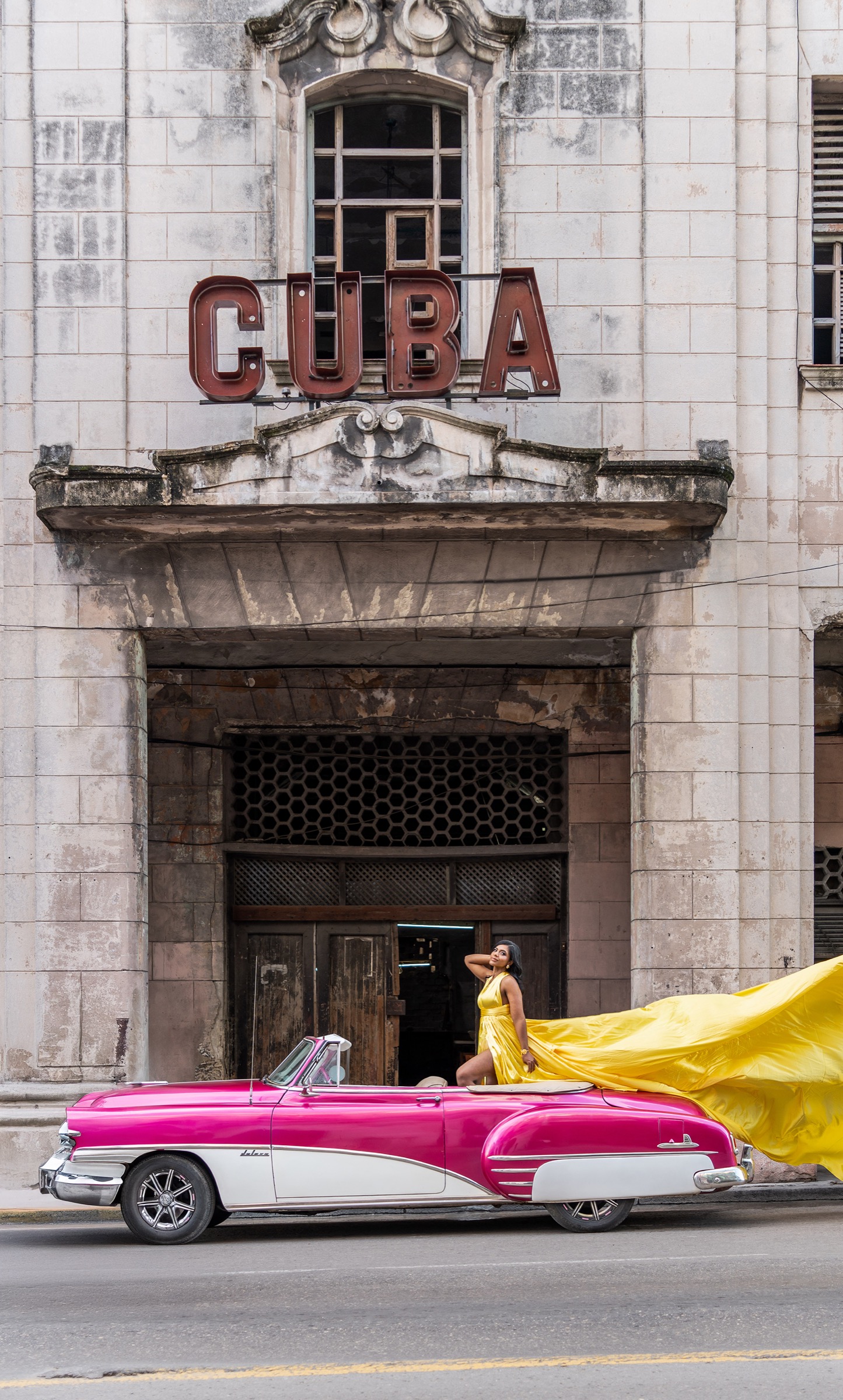 A woman in a yellow flying dress on a pink convertible at the cinema facade