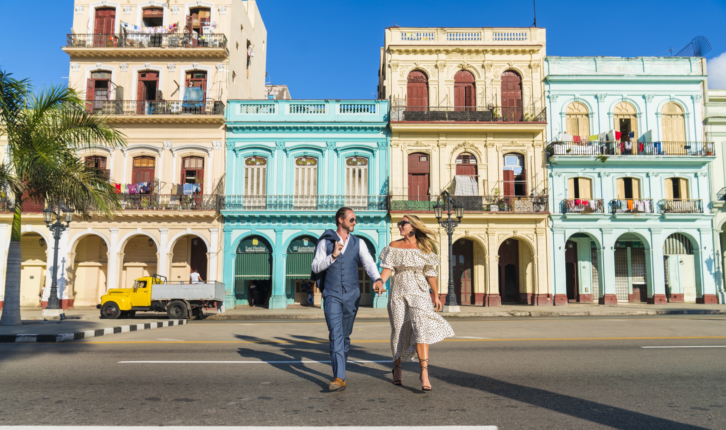 A couple walking across the crosswalk in front of Havana's colourful houses