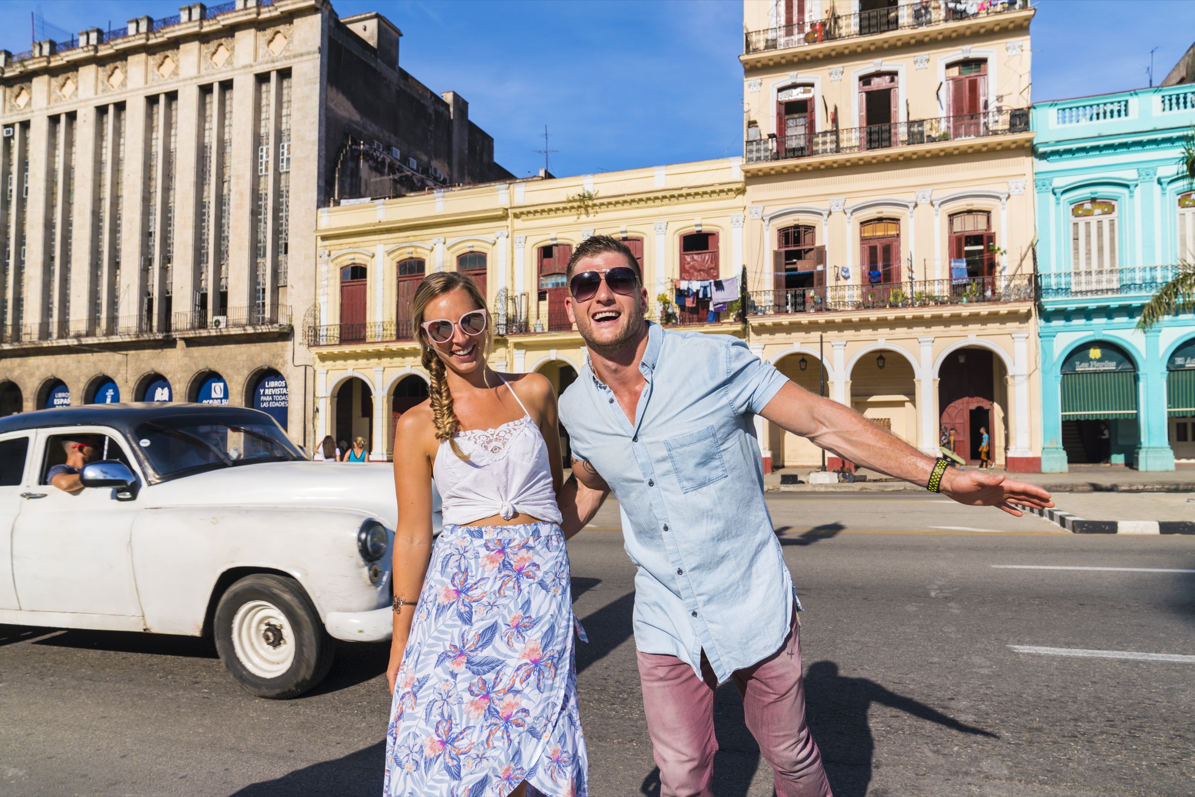 A couple laughing in the street, a white classic car beside them