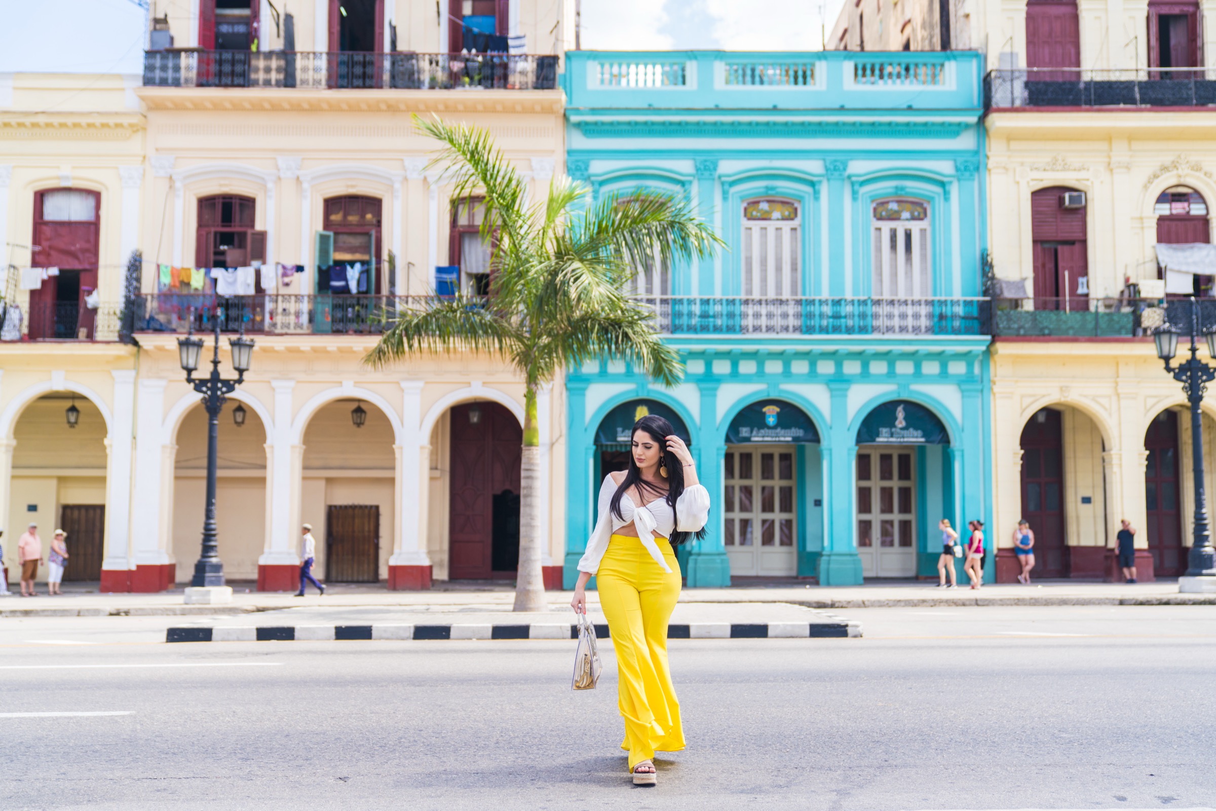 A woman in yellow trousers crossing the road in front of a turquoise building