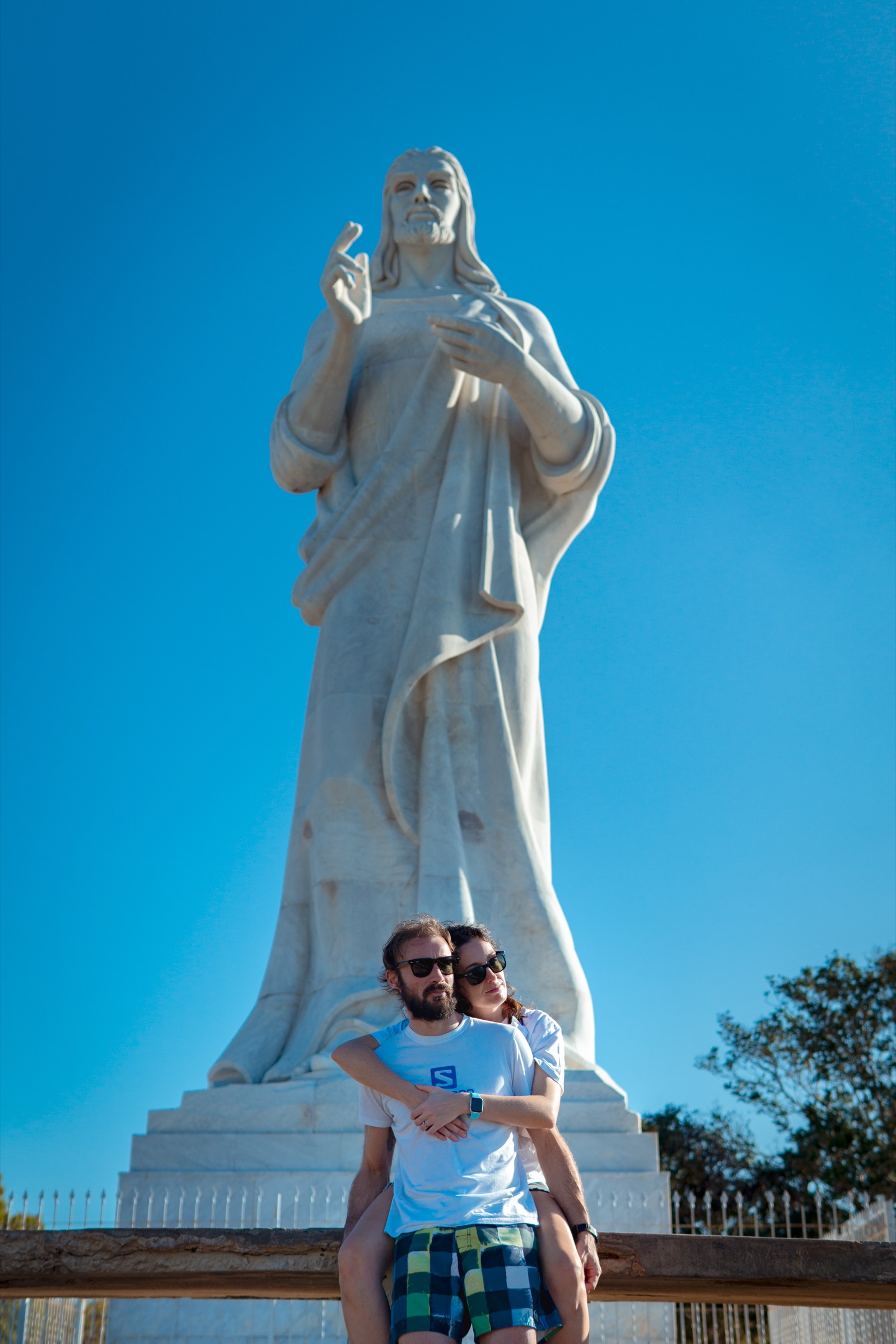 A couple embracing at the base of the white marble Christ statue against a blue sky