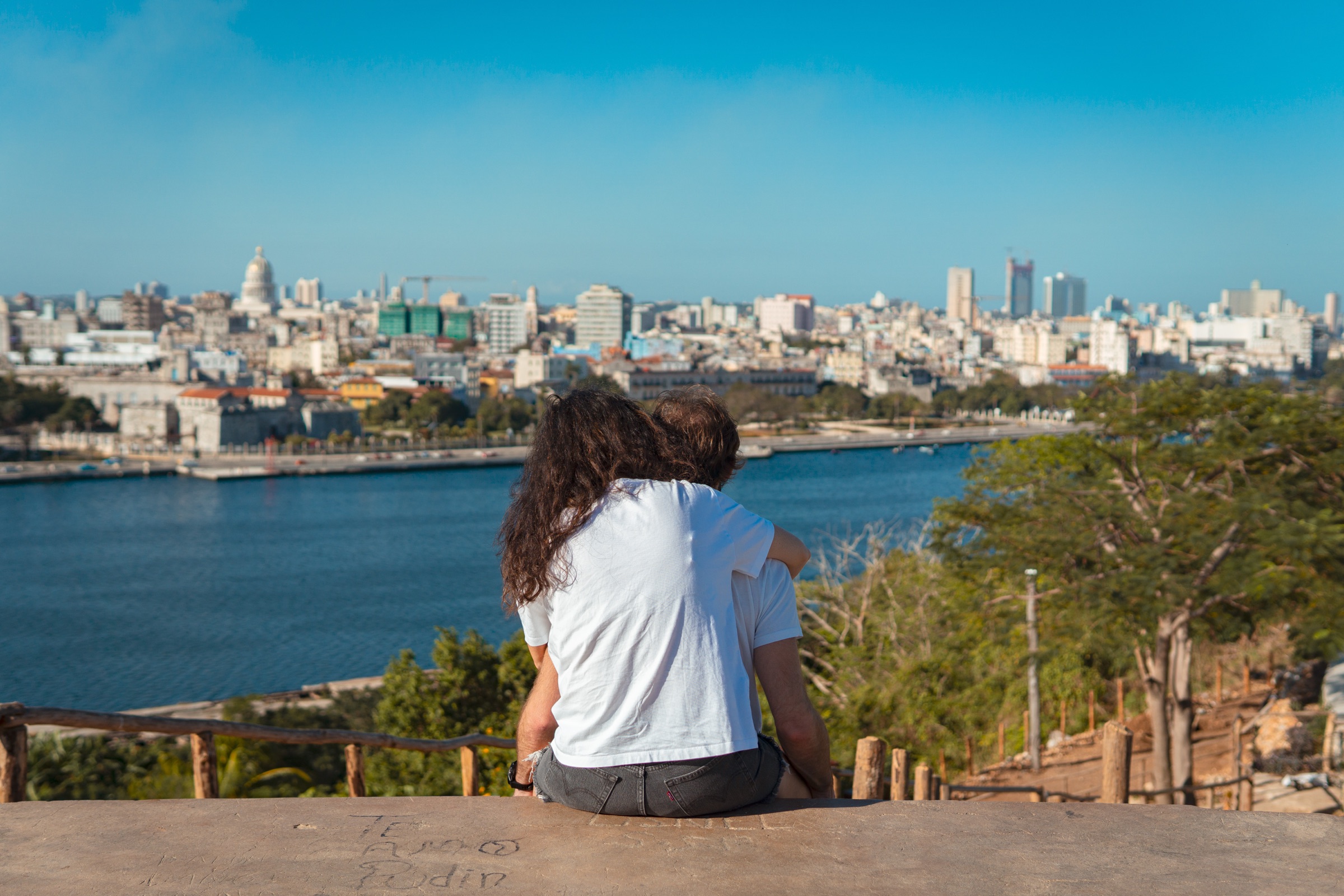A couple sitting on the overlook wall gazing at Havana bay and the city beyond