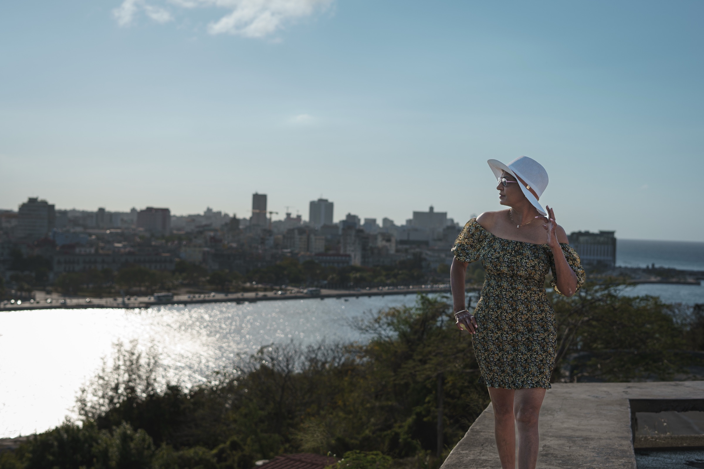 A woman in a white hat above the silvery bay in late light