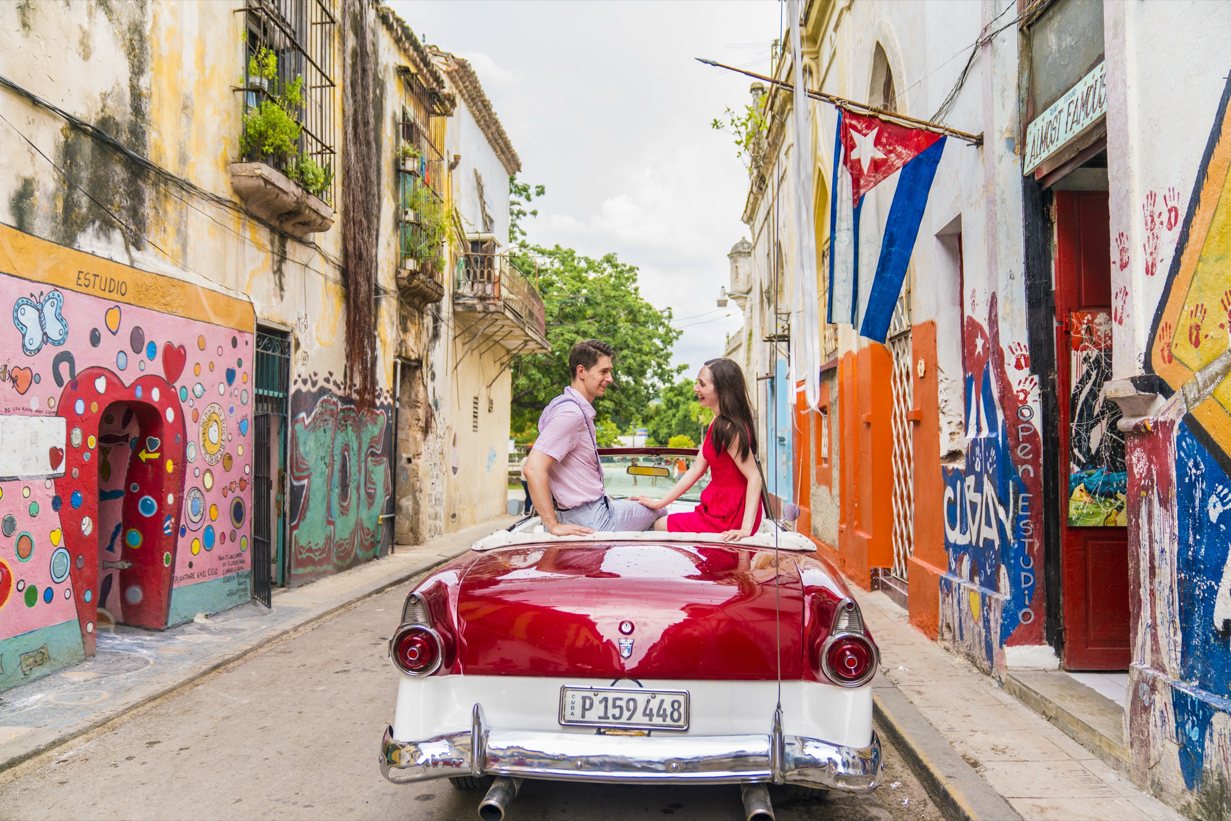 A couple in a red classic convertible on the colourful gallery street