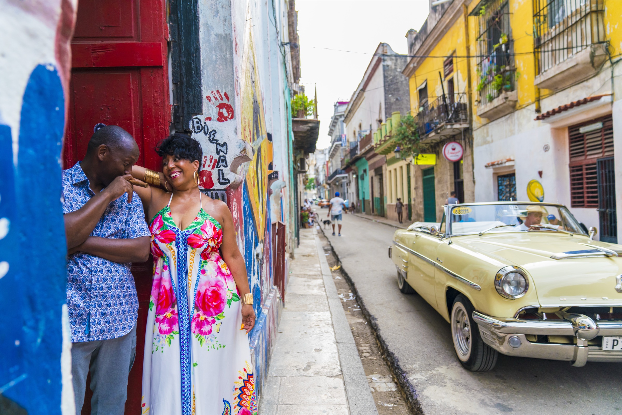 A couple beside a painted wall, a yellow classic car on the gallery street