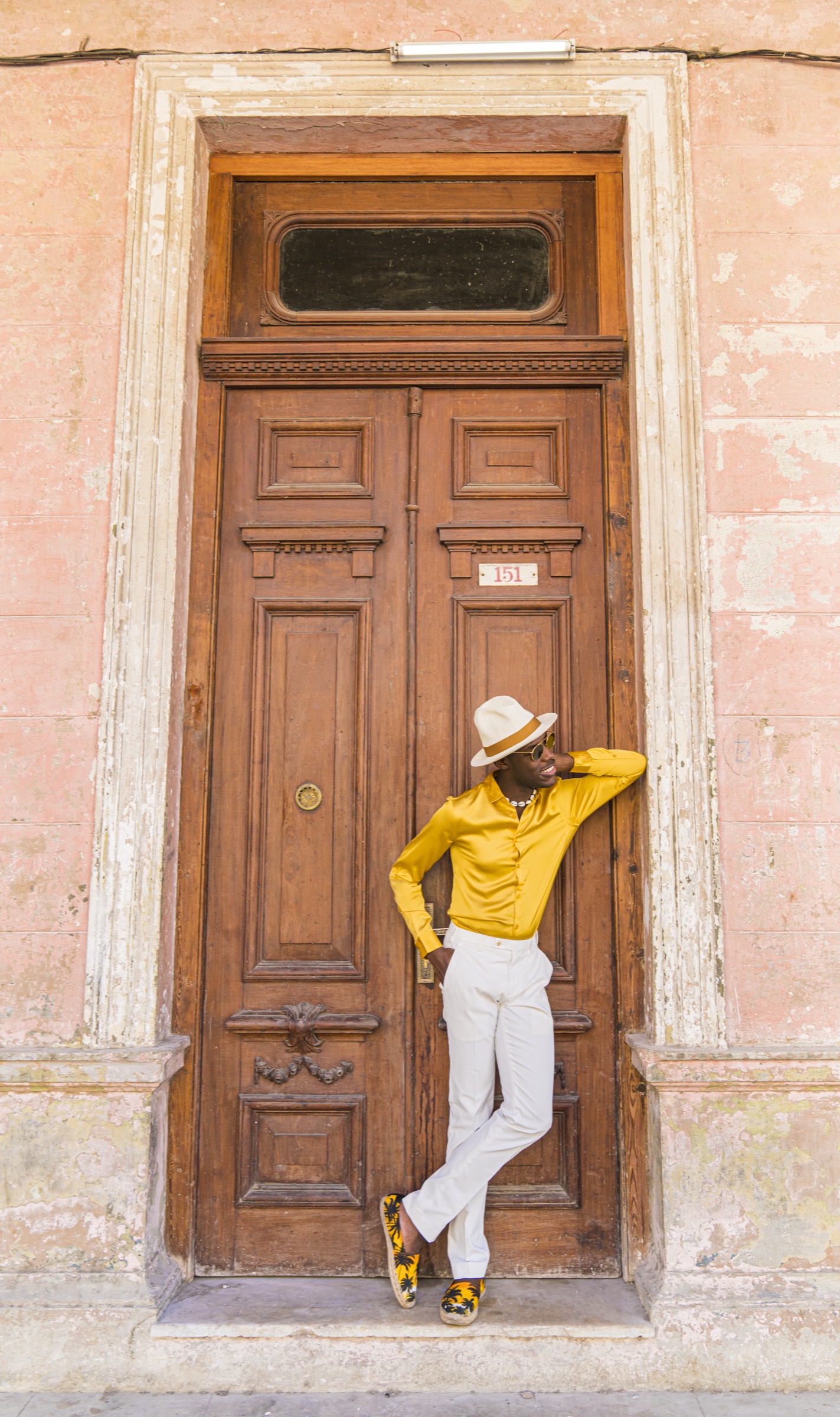 A man in a yellow shirt leaning against a tall weathered wooden door