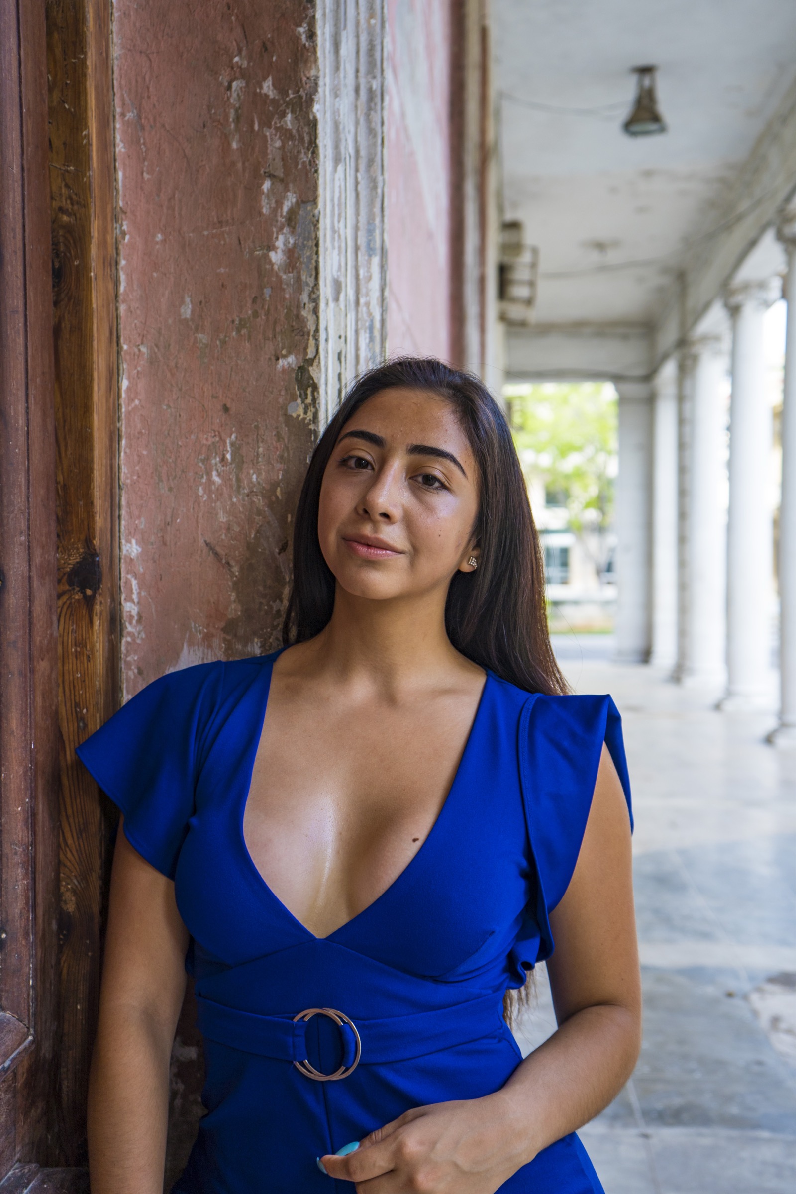 A woman in a blue dress leaning against a weathered doorframe and column