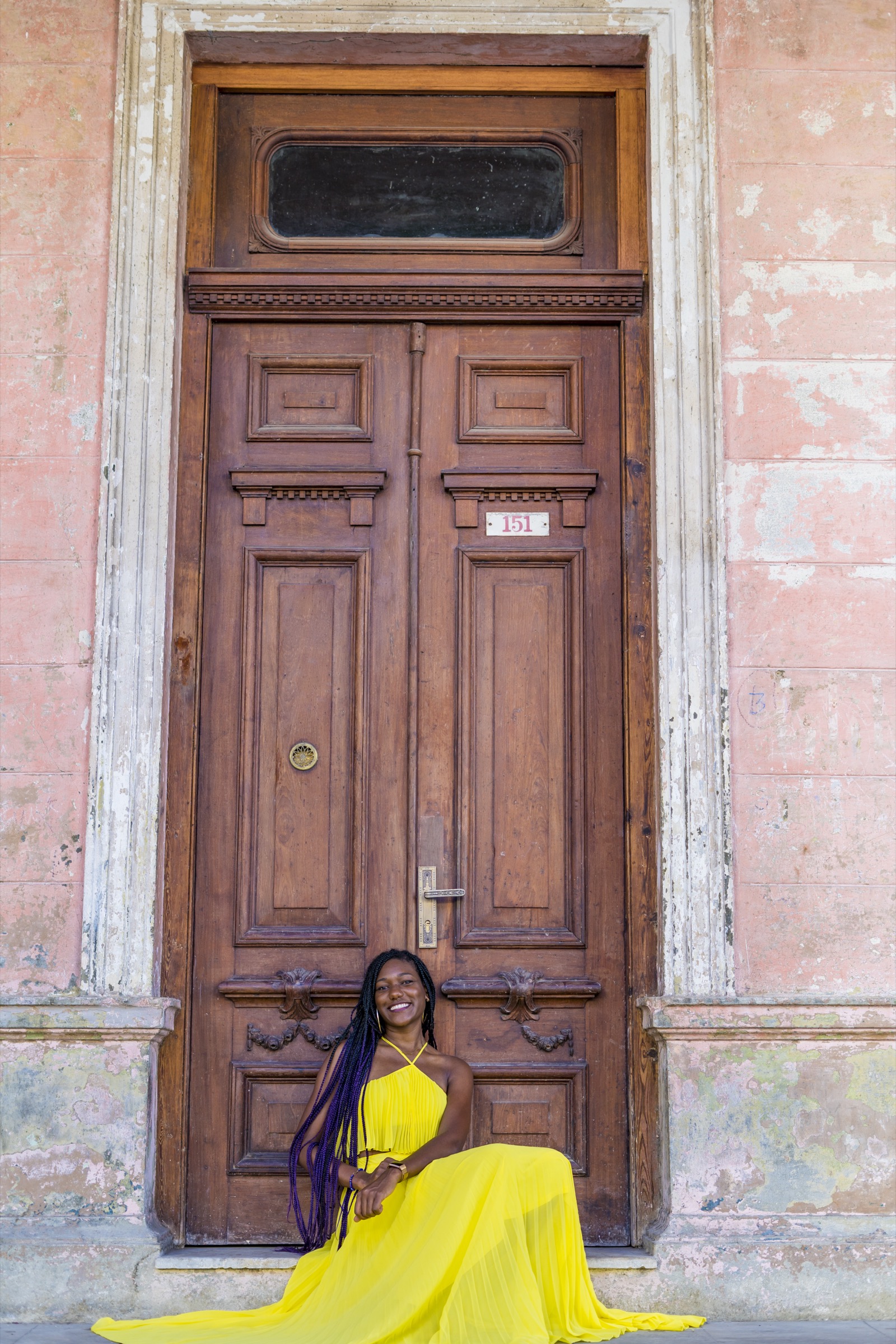 A woman in a yellow dress seated in front of a tall wooden door