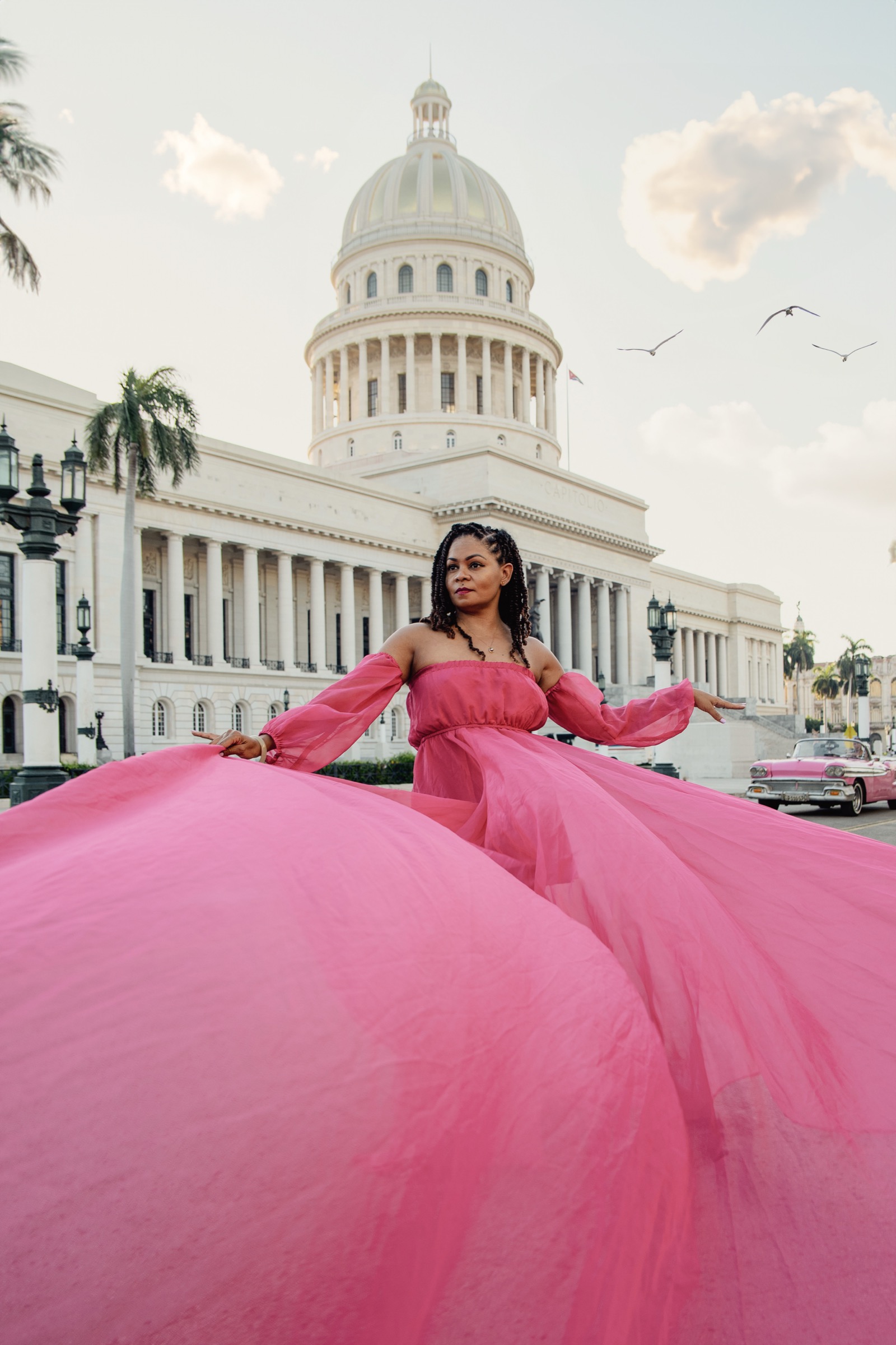 A woman in a flowing pink gown twirling in front of El Capitolio at sunset