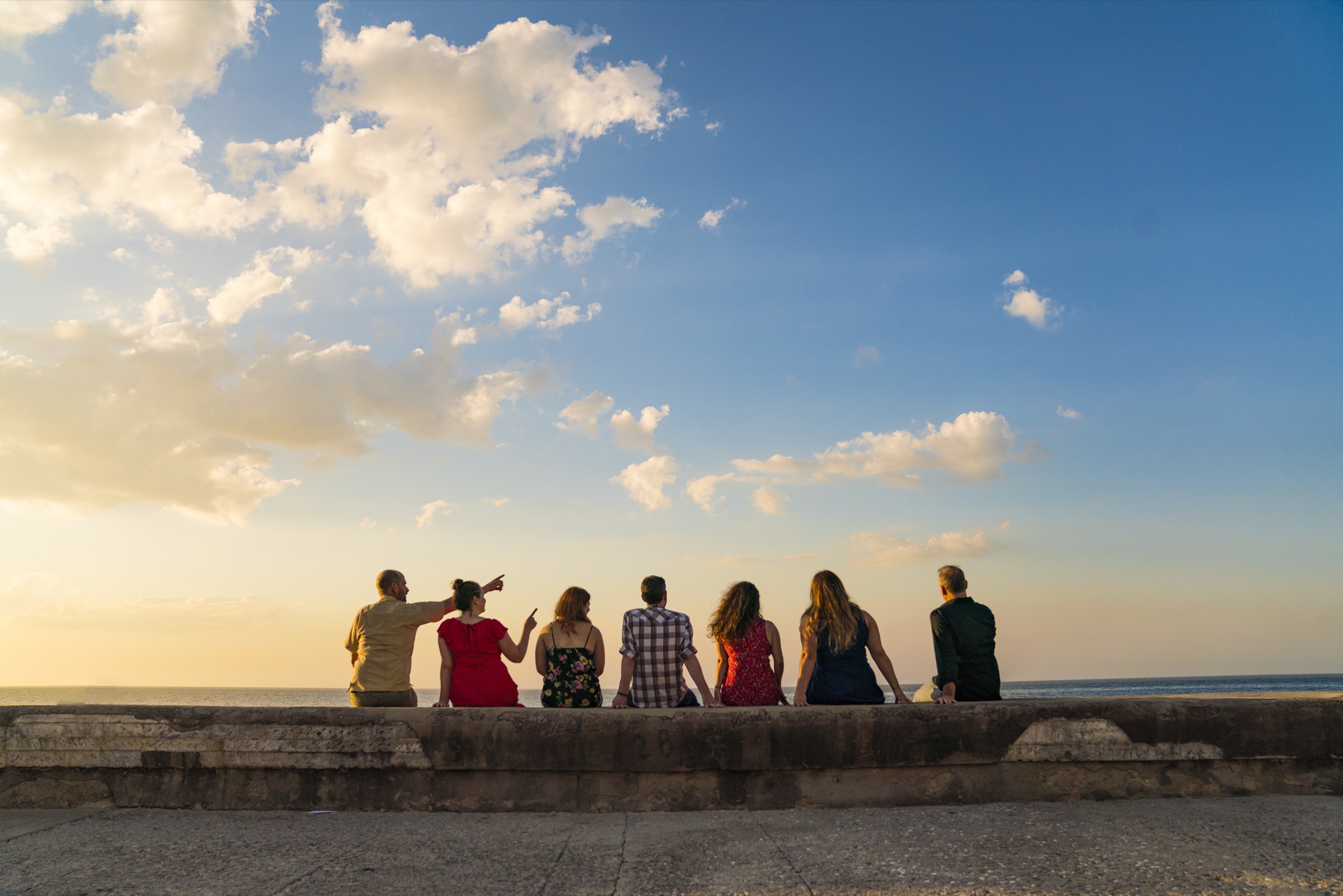 A group of friends sitting on the Malecón seawall at sunset