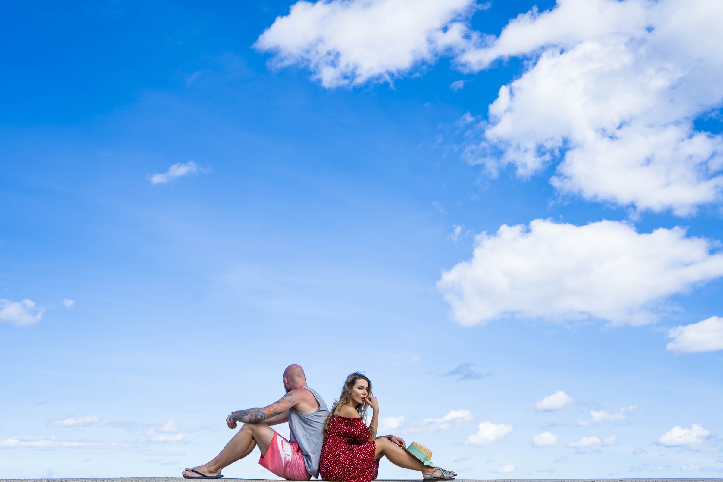 A couple sitting back to back on the seawall, a vast sky above them