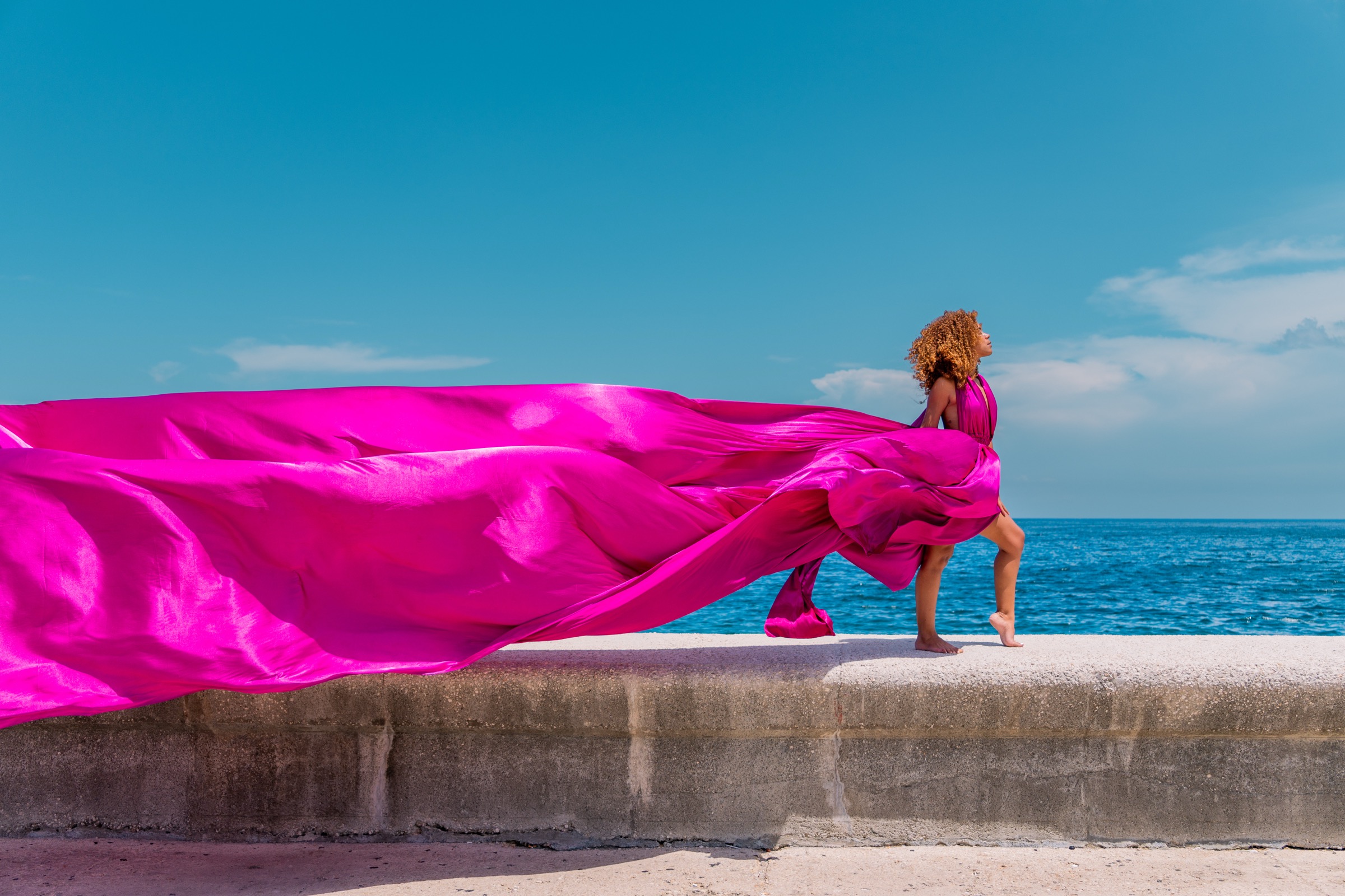 A woman in a flowing magenta gown on the seawall, a Flying Dress shoot
