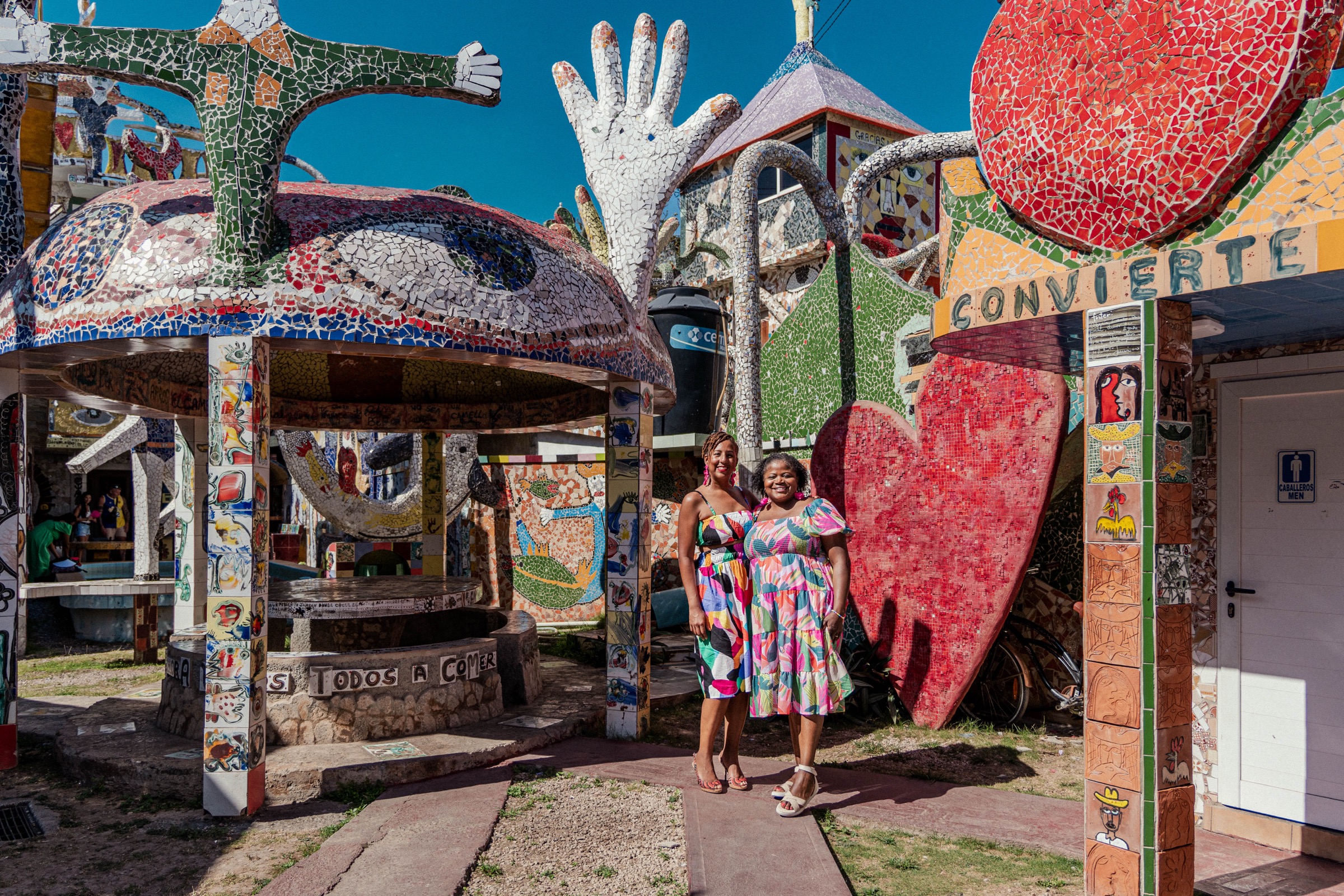 Two women in front of Fuster's red mosaic heart and white hands sculpture
