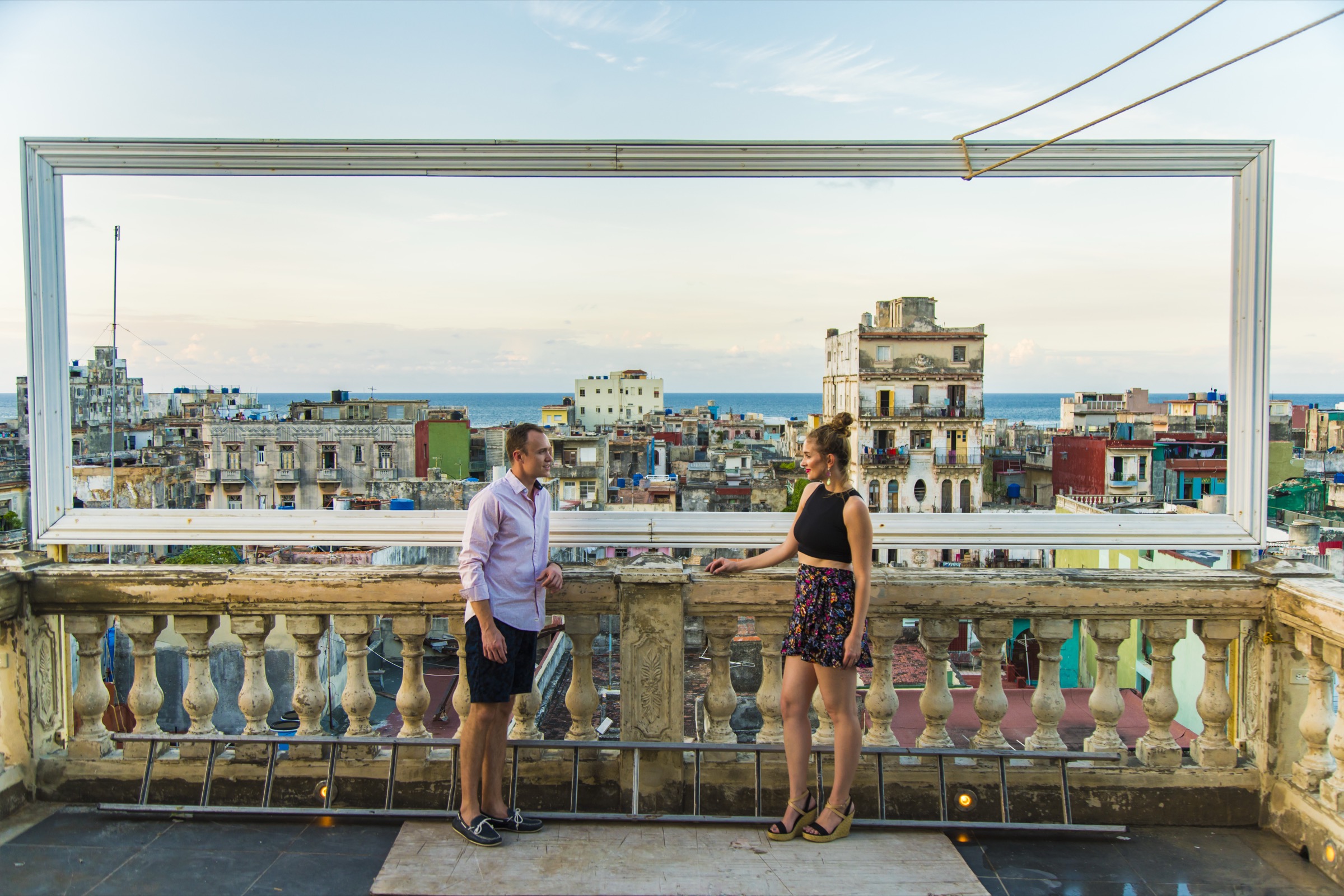 A couple at the painted frame on La Guarida's rooftop, Centro Habana skyline framed inside