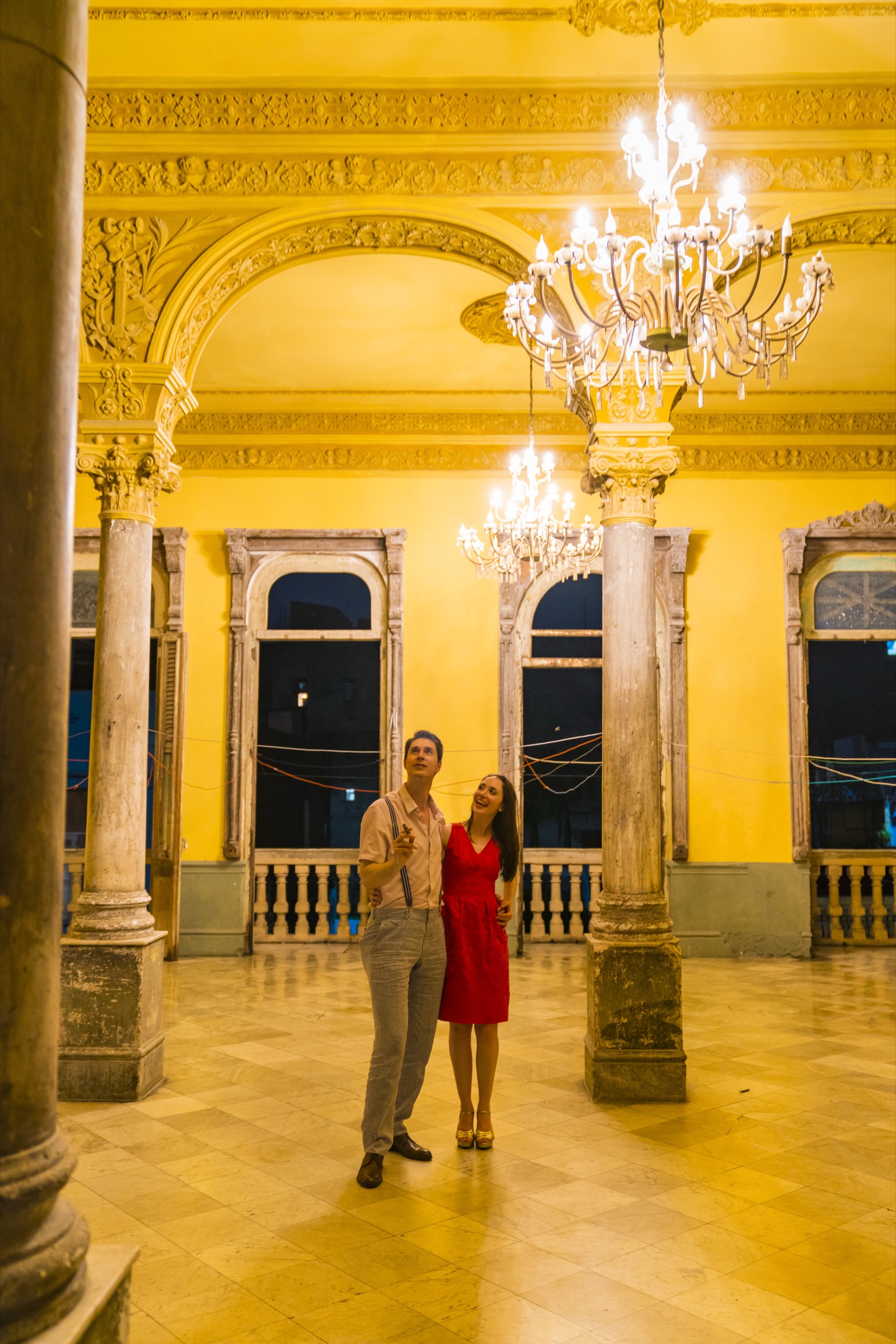 A couple under chandeliers in the faded grand ballroom with yellow columns