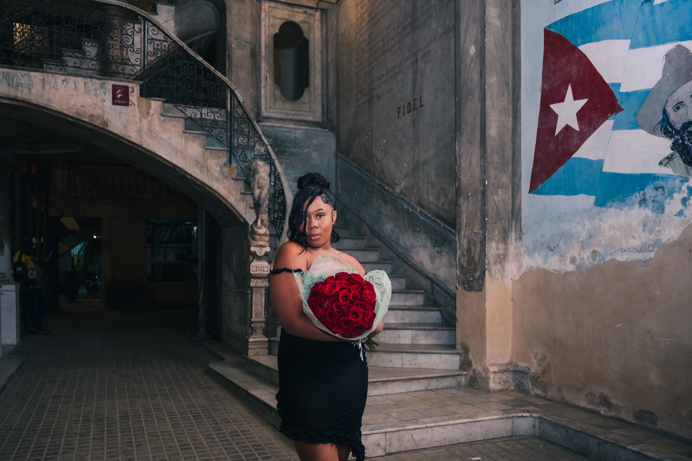 A woman in black holding red roses by the spiral staircase and painted Cuban flag