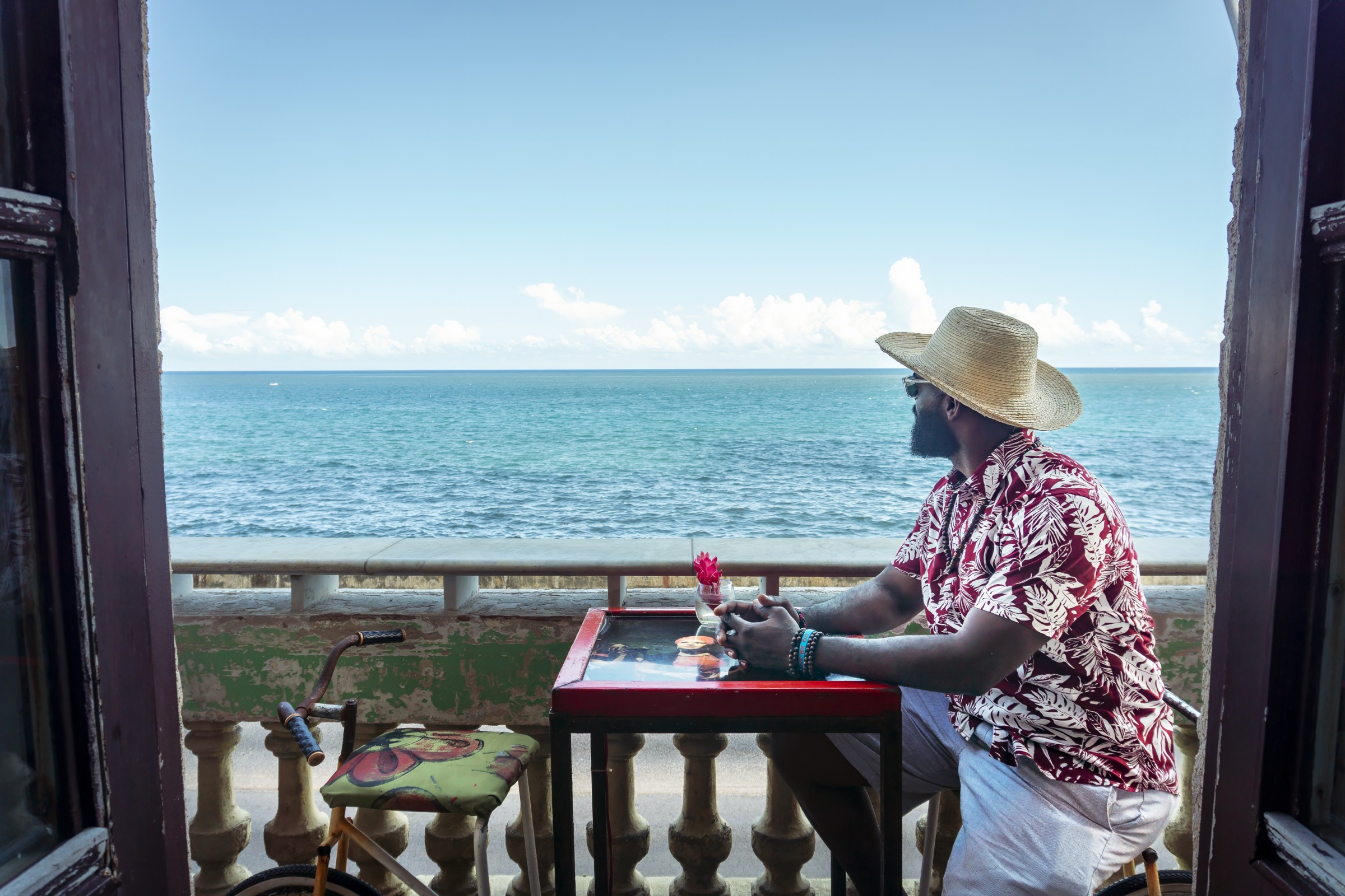 A man in a printed shirt at a balcony table looking out over the seawall