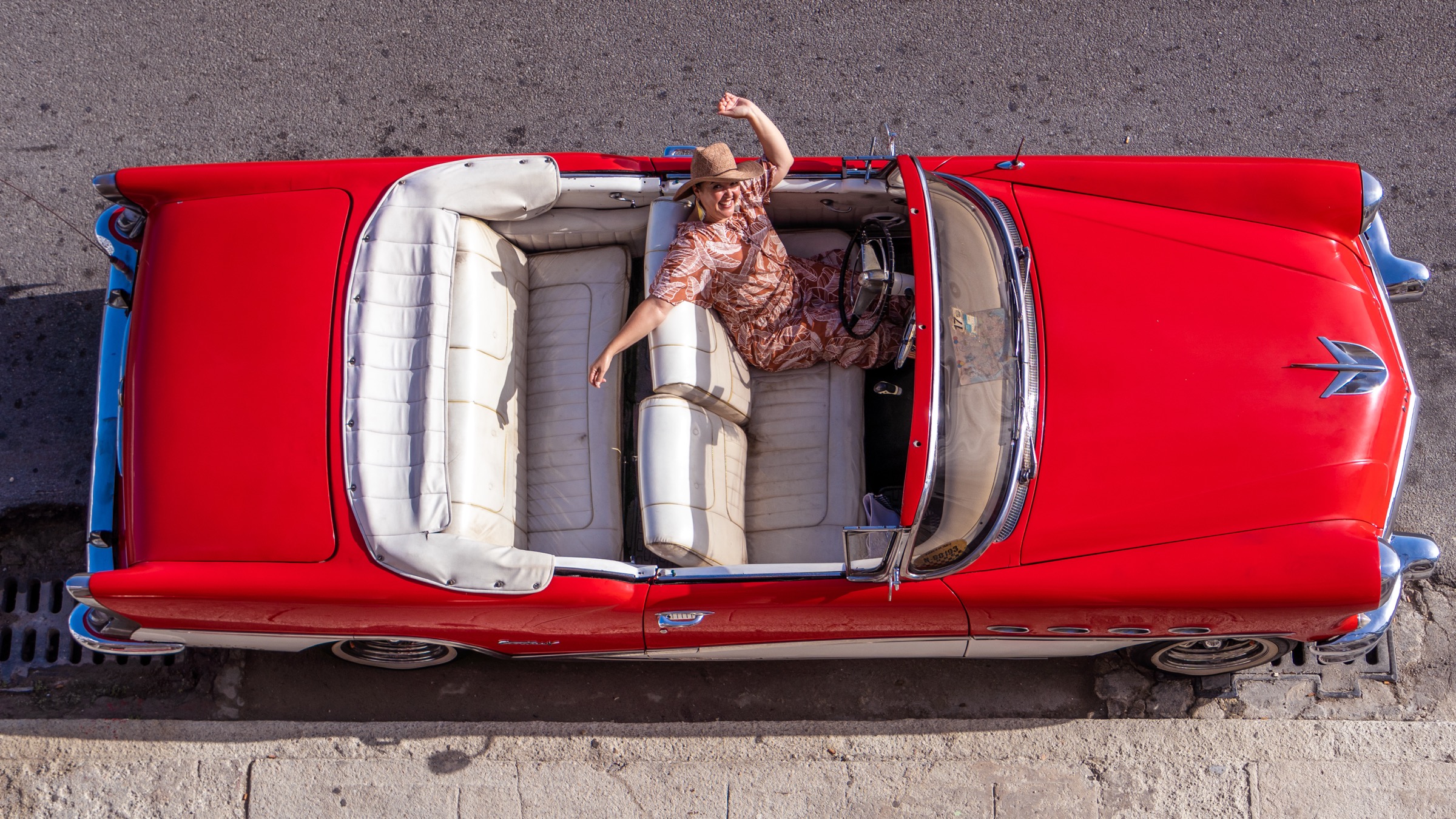 An overhead shot of a woman posing in a red classic convertible from above