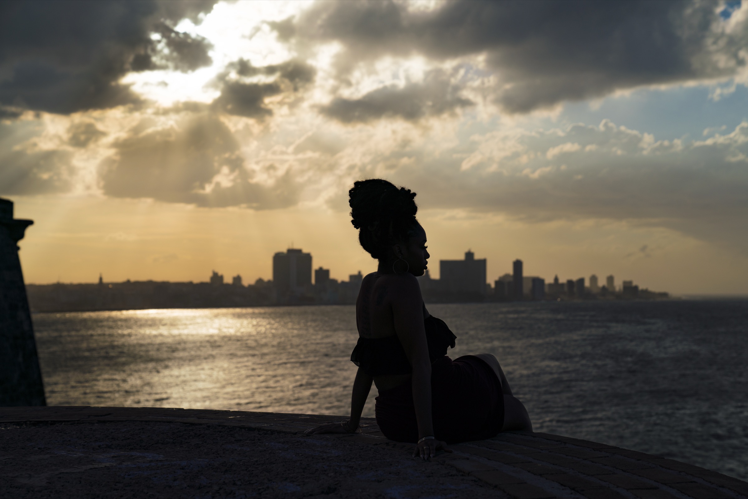 A woman in silhouette on the ramparts, the Havana skyline backlit at sunset