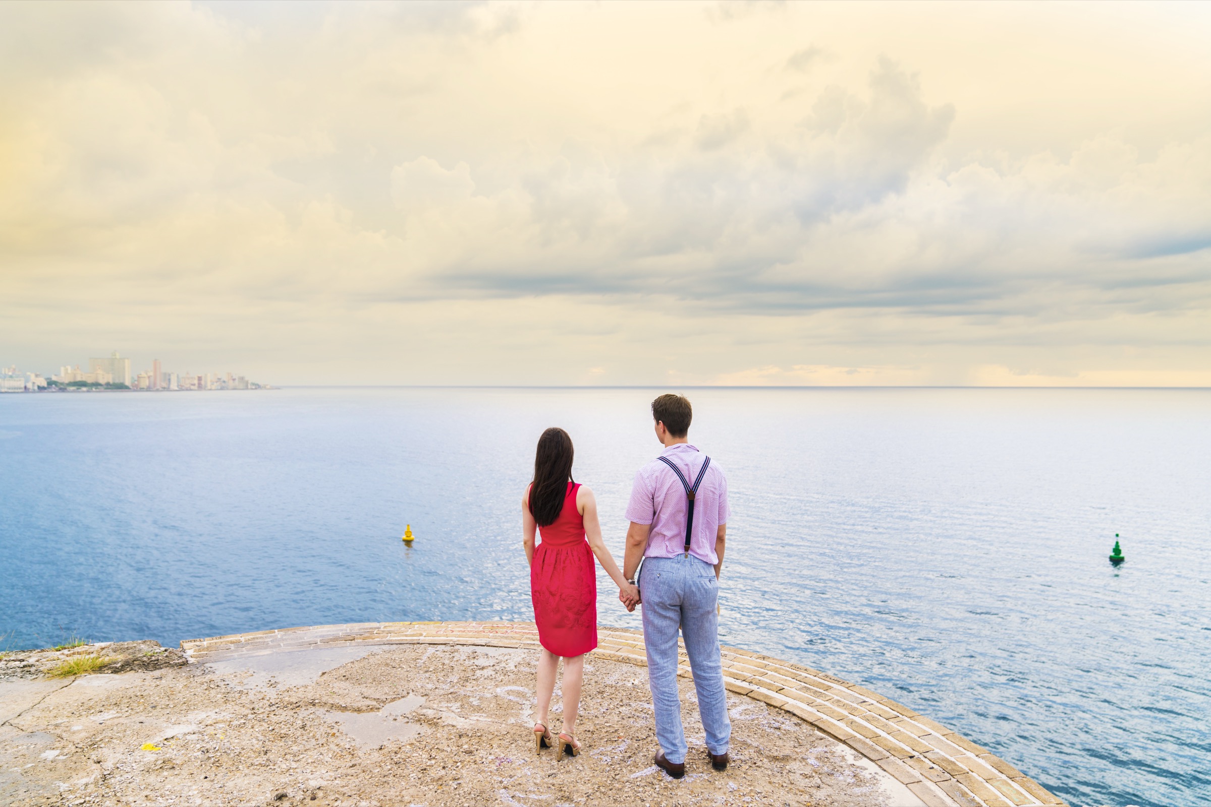 A couple standing back to the camera, facing the sea under a vast cloudy sky