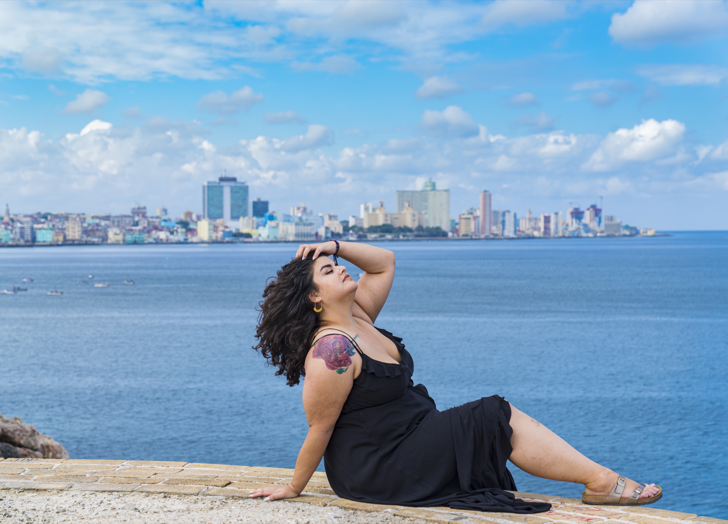 A woman reclining on the rampart wall, the Havana skyline across the water