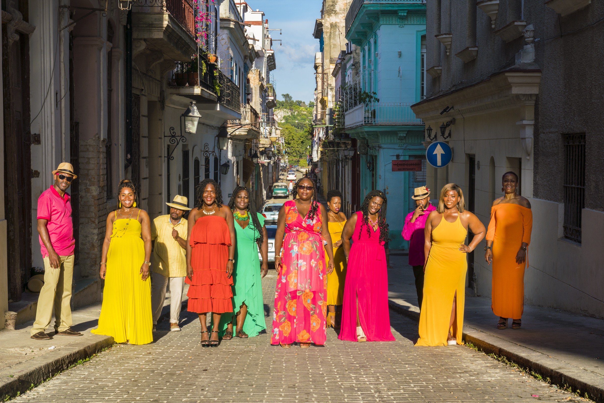 A large group in colourful dresses standing along the cobbled lane