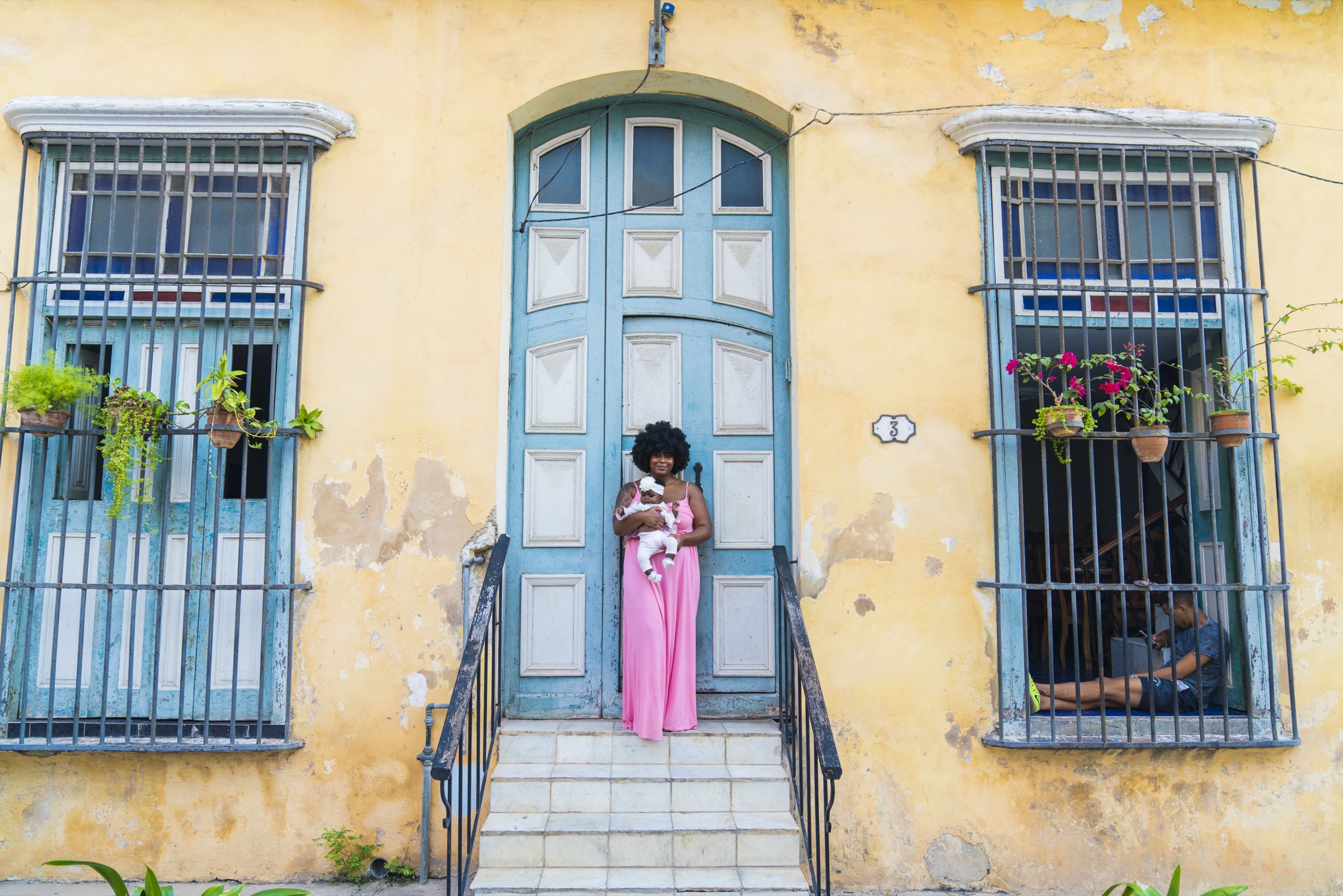 A woman in a pink dress in a blue doorway on the yellow wall